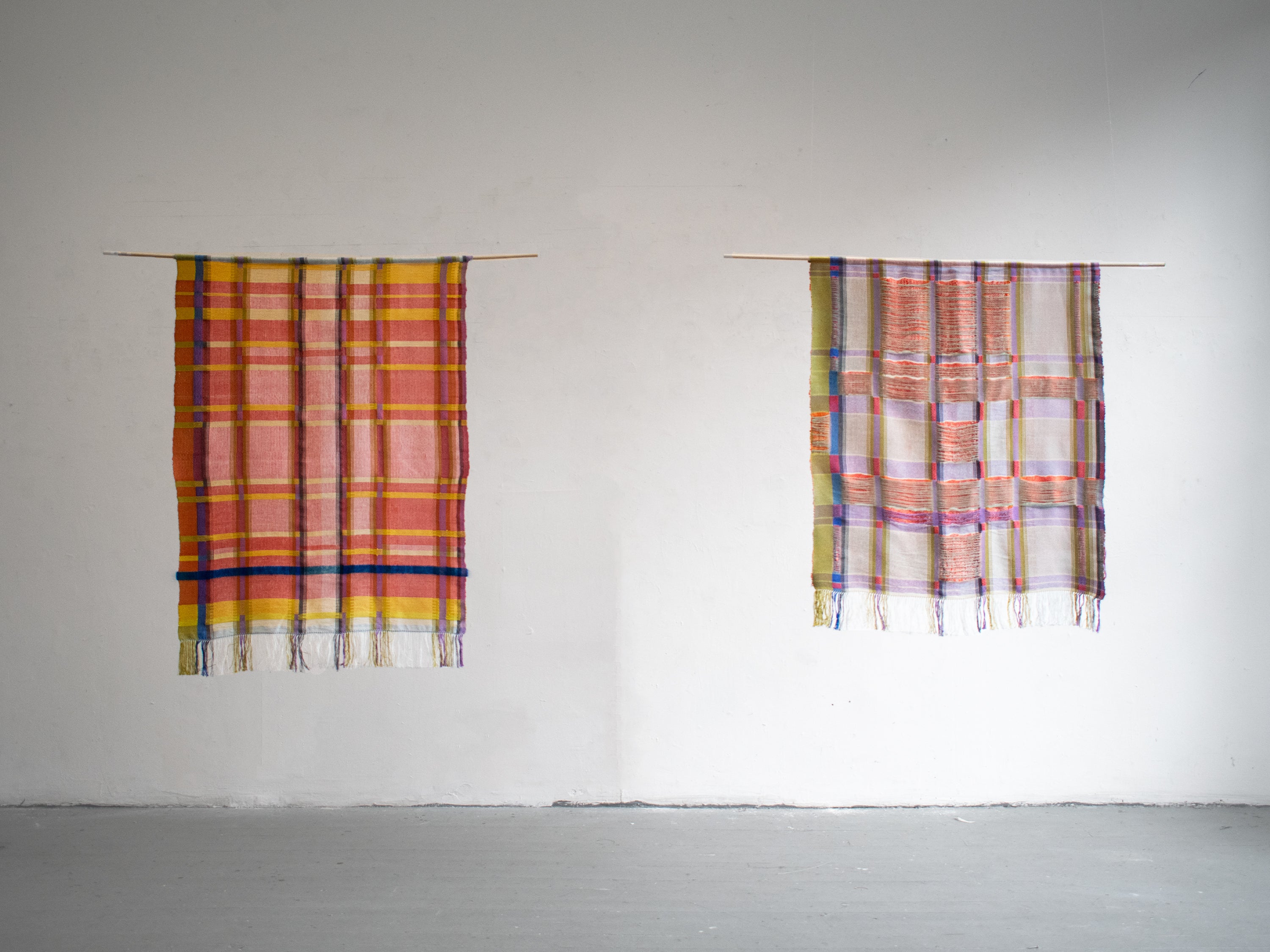 Two handwoven textiles hung side by side, each depicting a pattern derived from an Italian Renaissance building. The pieces mirror one another with an unsettling, near-identical symmetry