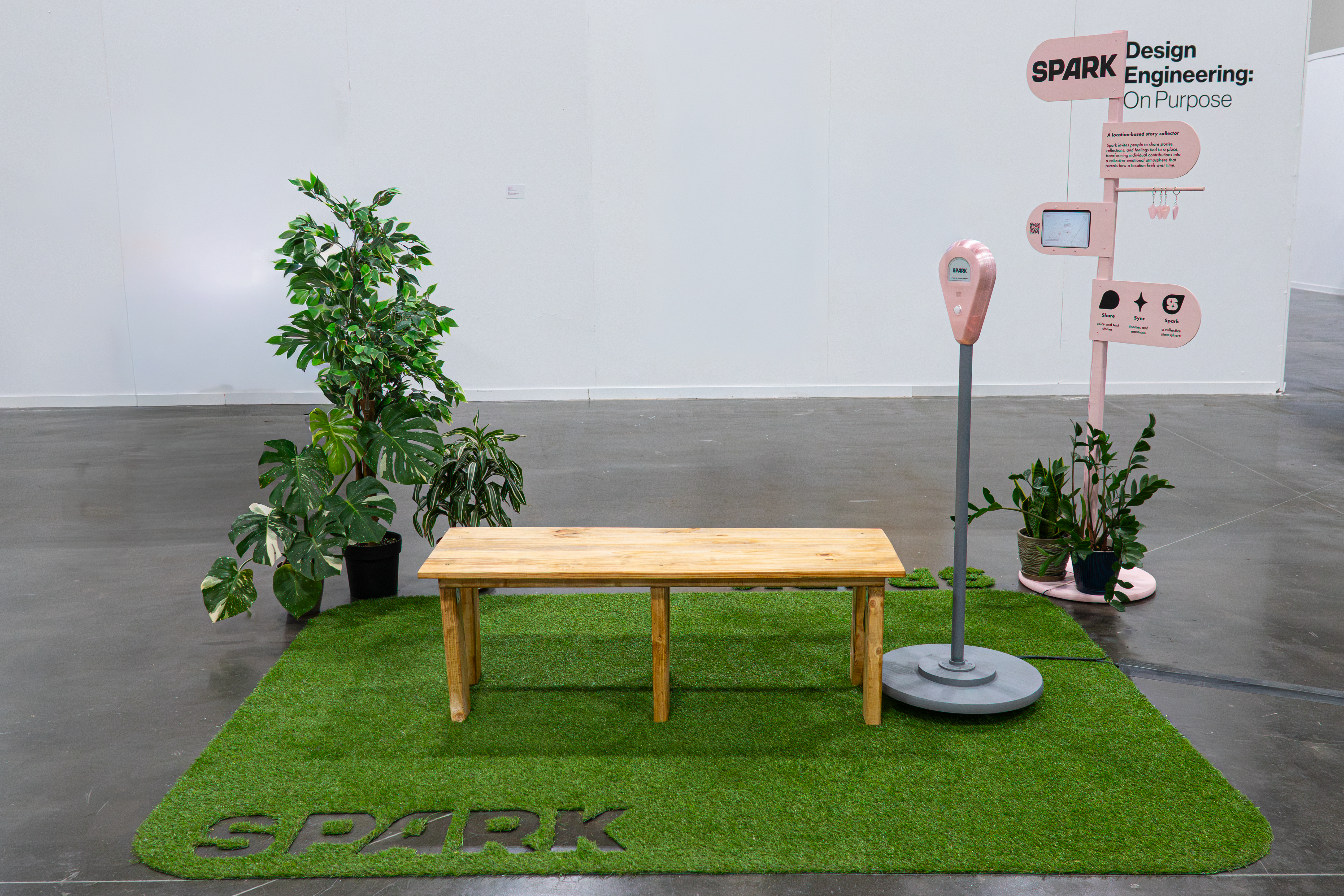 Spark exhibition setup with artificial grass, wooden bench, plants, and signage.