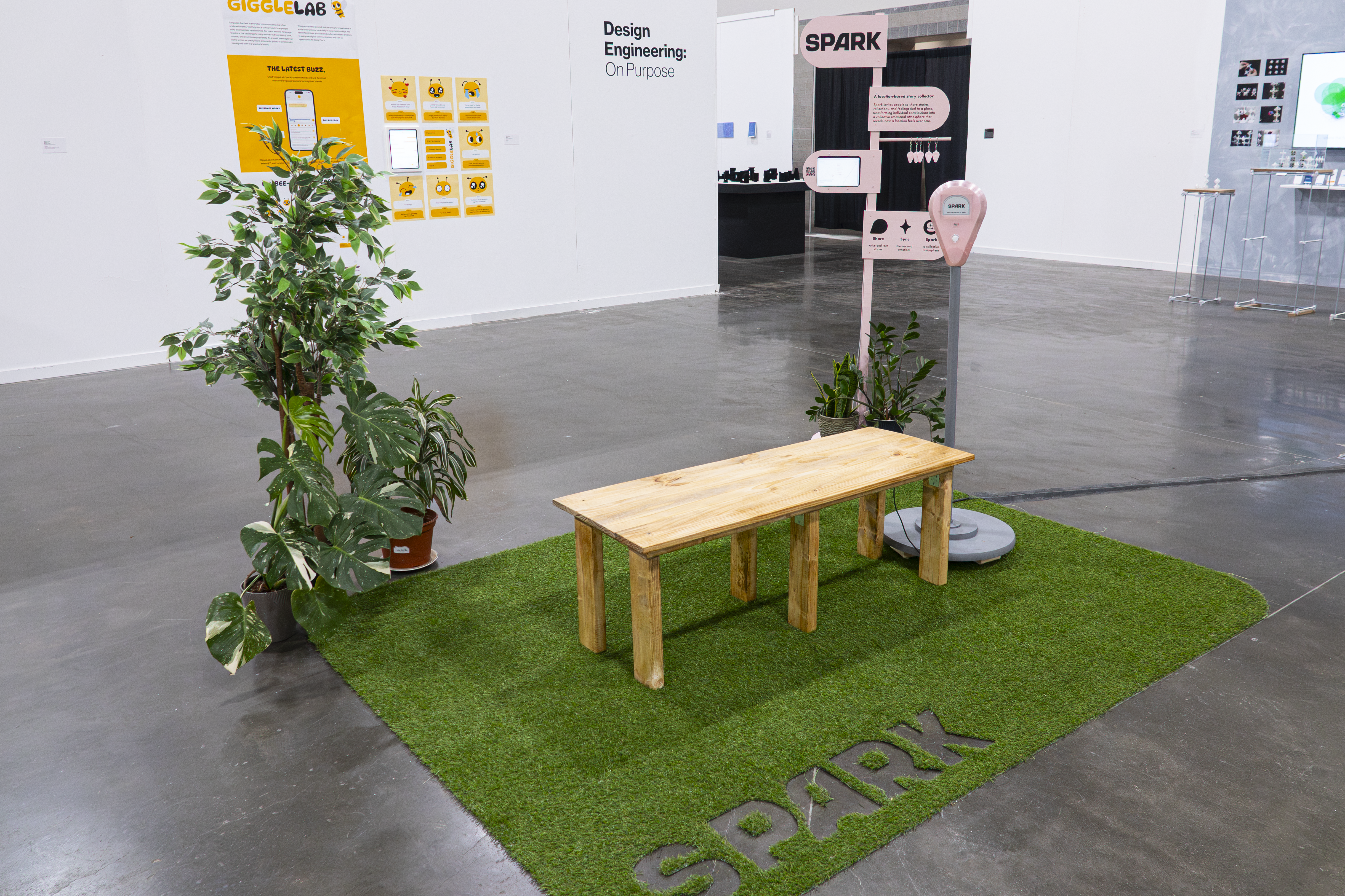 Angled view of Spark exhibition setup with artificial grass, wooden bench, plants, and signage.