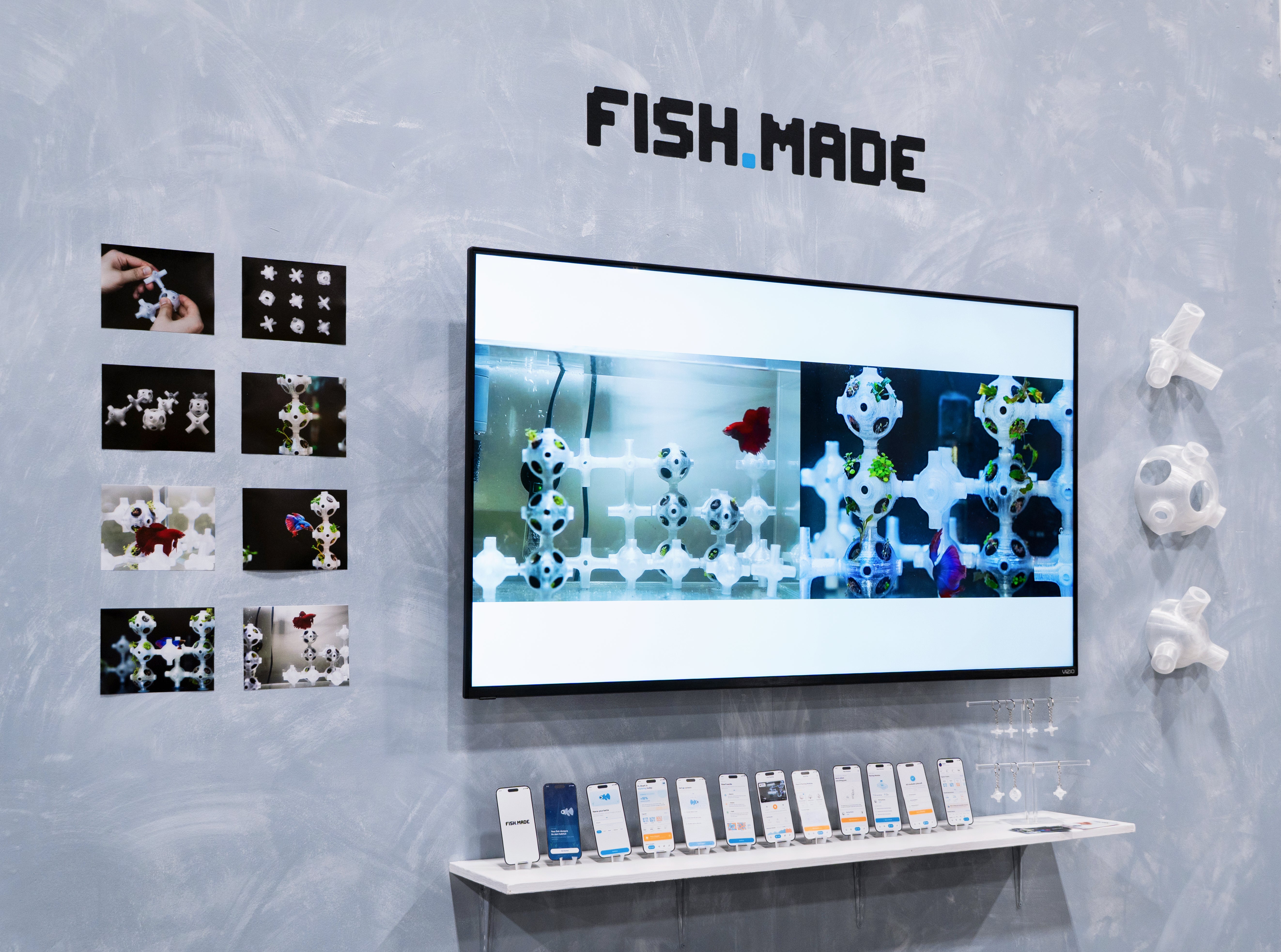 FISH.MADE exhibition setup featuring a screen with generated habitat structures, a fish tank prototype, modular 3D-printed components, and app interface mockups.