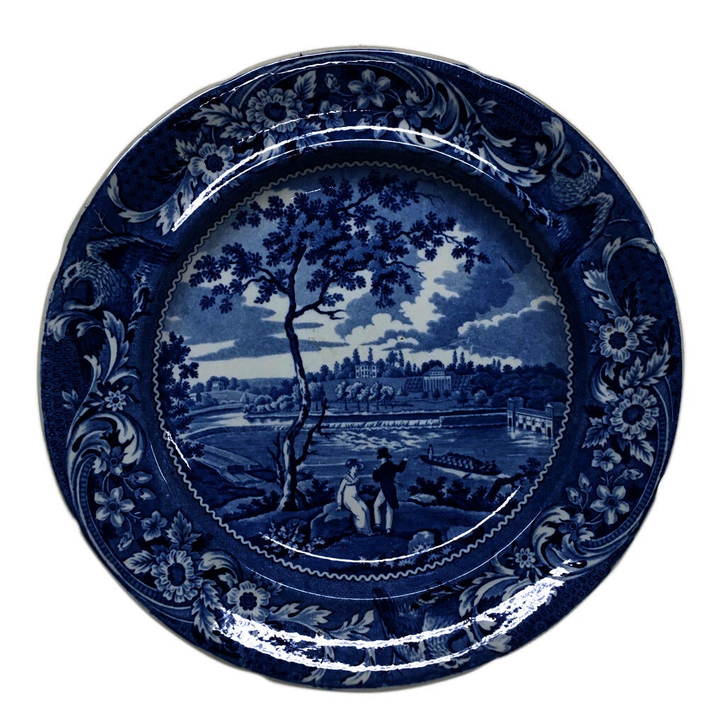 blue and white transferware plate depicting a scene near Philadelphia with two figures sitting by a tree, looking at a waterway
