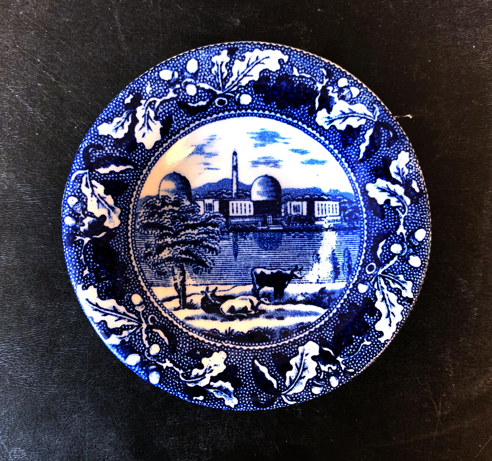 blue and white transferware cup plate depicting a the indian point nuclear power plant and cows, with an oak leaf border