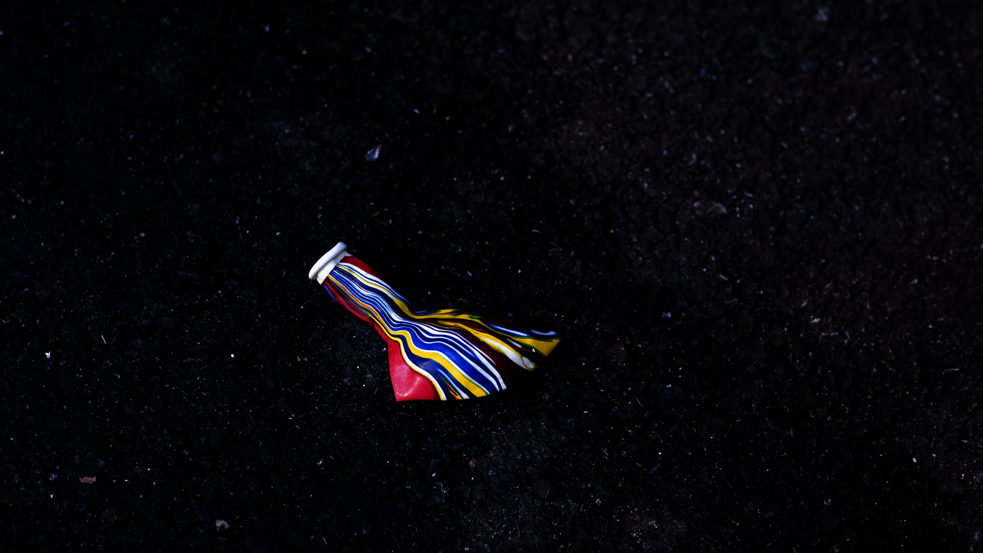 deflated rainbow balloon on black asphalt