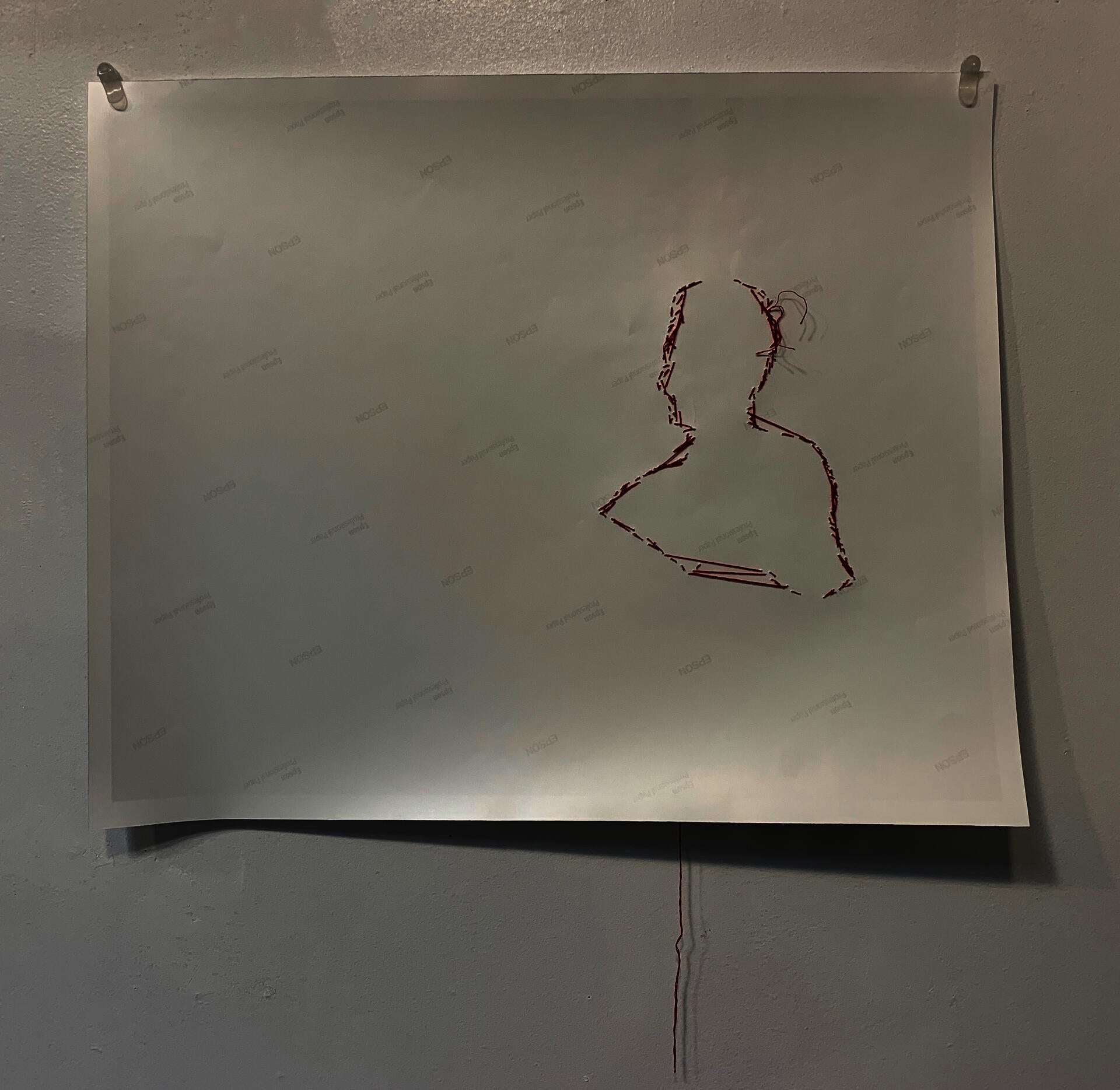 Red thread creates the outline of a figure on the back of photo paper