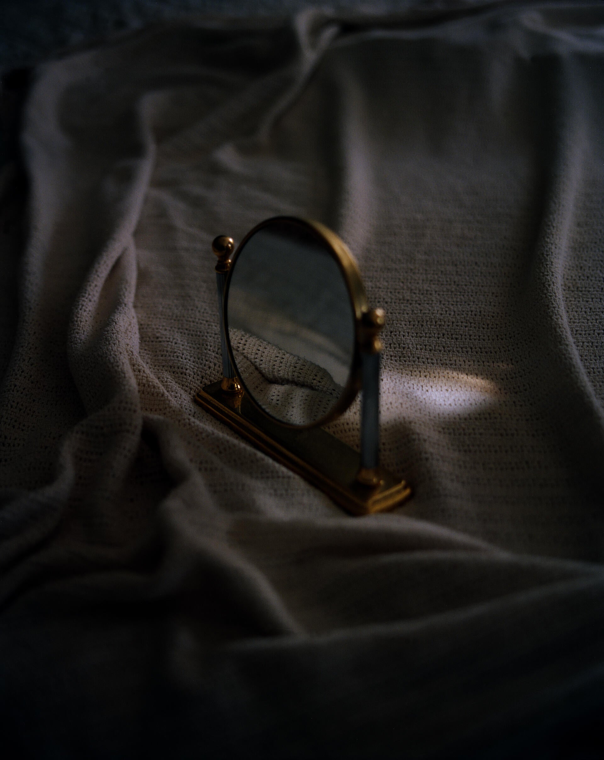 A small mirror stands on a bed, reflecting the rumpled sheets