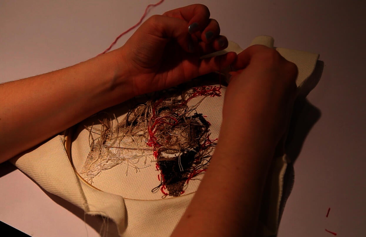 A person ties a knot on the back of an embroidery hoop