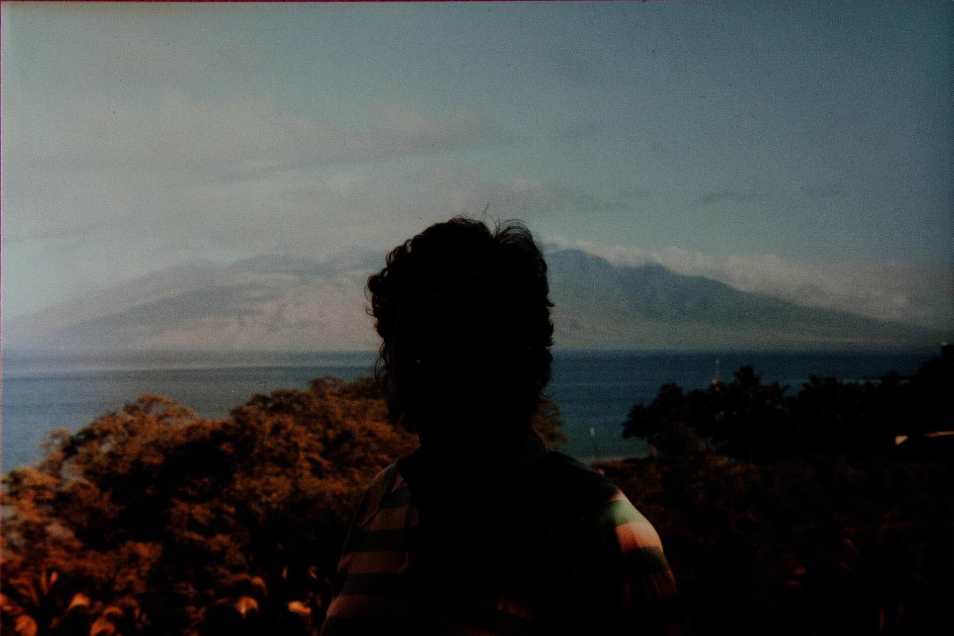 A color photograph in which a landscape can be seen behind a severely underexposed and backlit person.