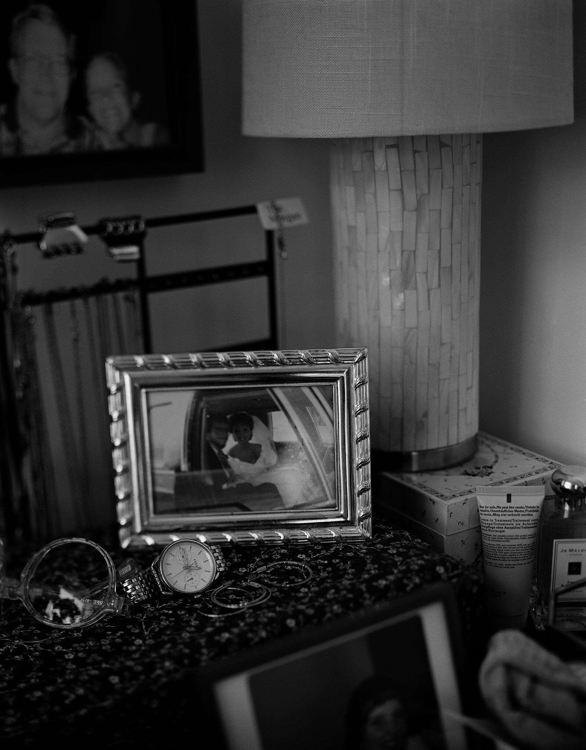 Black and white photograph of a wedding picture from the 1980s in a silver frame, on top of a dresser.