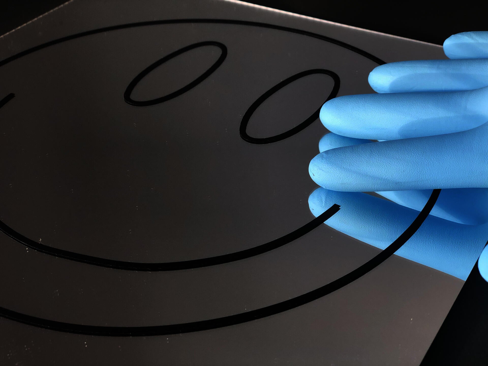 Smiley face graphic on a mirror with a blue-gloved hand