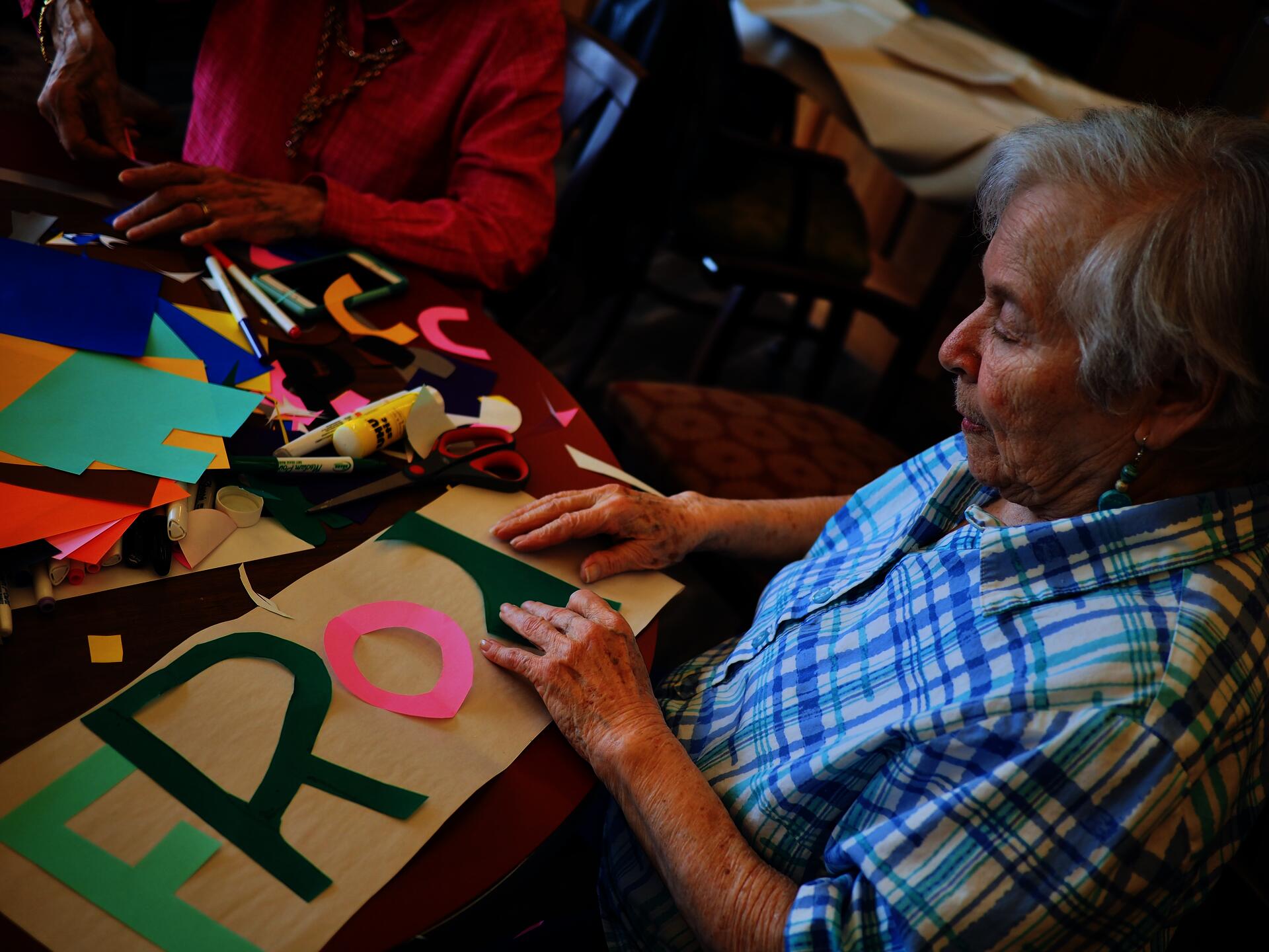 Image of an older female participant, sitting at a table and arranging brightly colored, cutout letters on a poster.