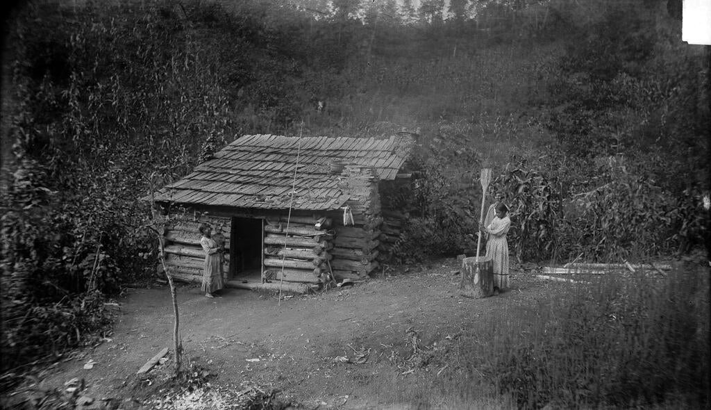 Photograph of Cherokee Medicine Man, Ayunini Swimmer, and his Log Cabin taken by James Mooney (1888).