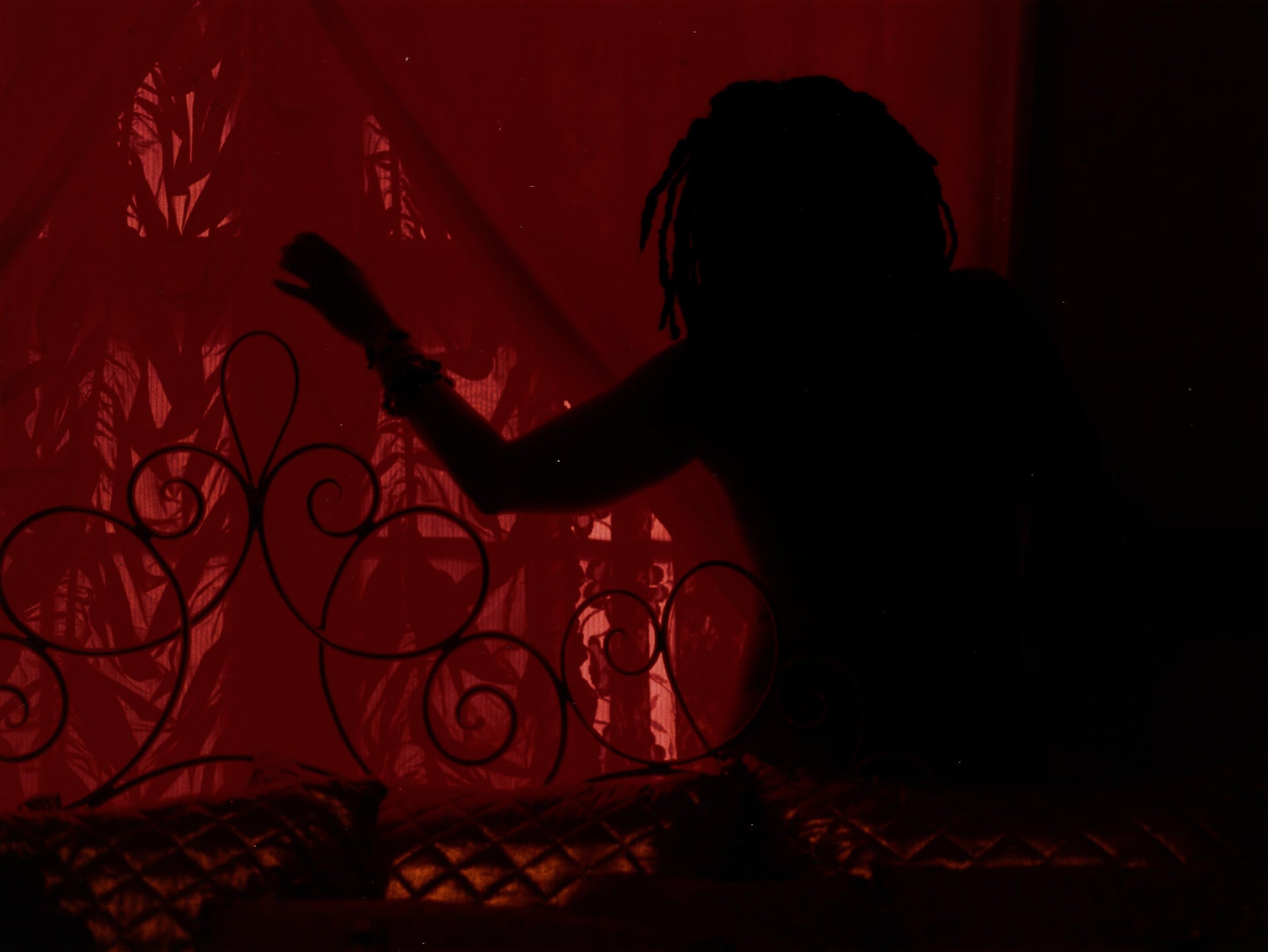 Photograph of a person with outstretched arm sillhouetted against a red window