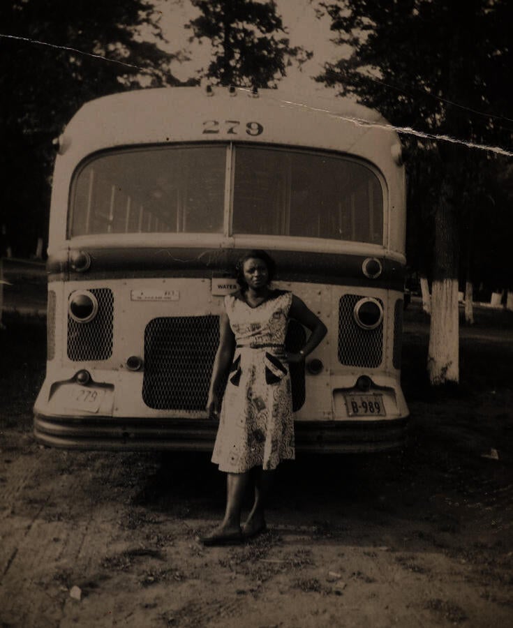 1940s black and white picture of a Black woman standing casually in front of a bus