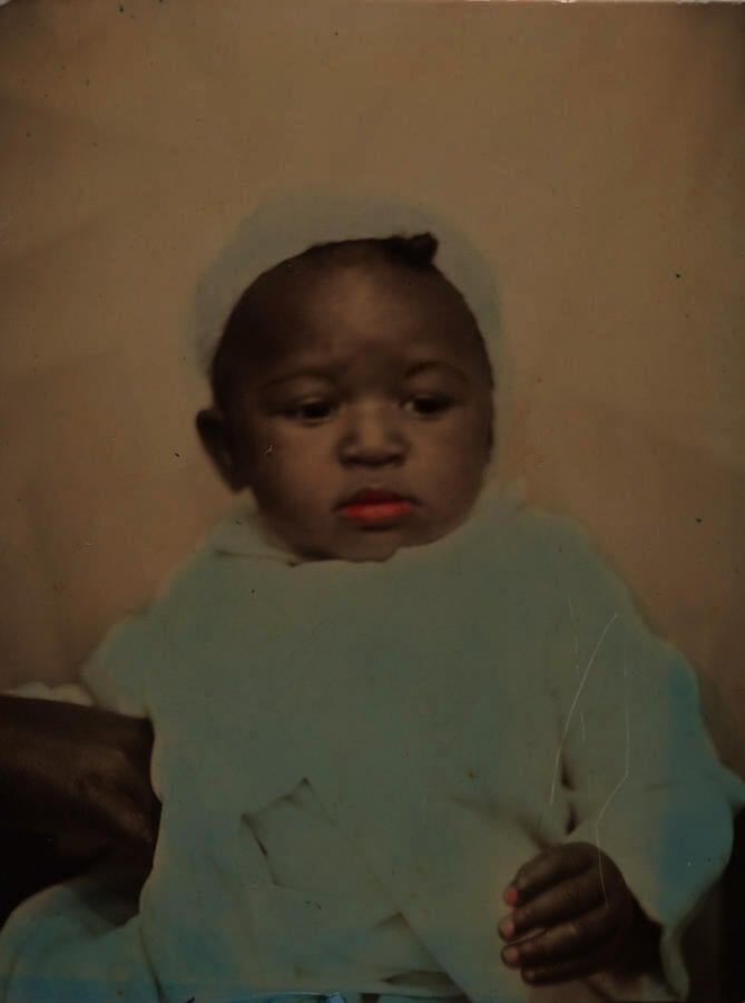 Black & white photograph of a baby, with its lips colored red and its clothes colored blue