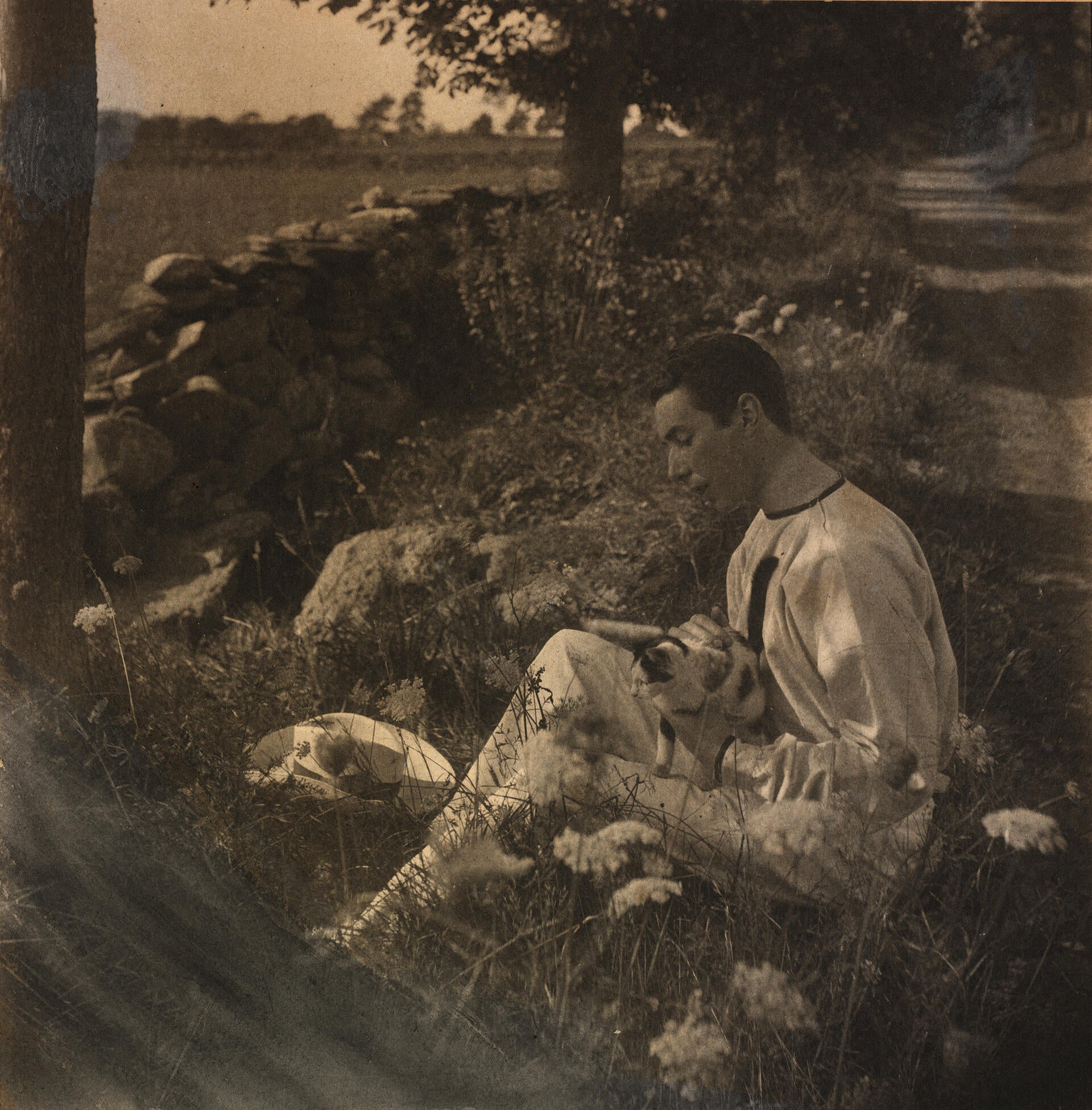 Sepia photograph of a man holding a cat on a country road