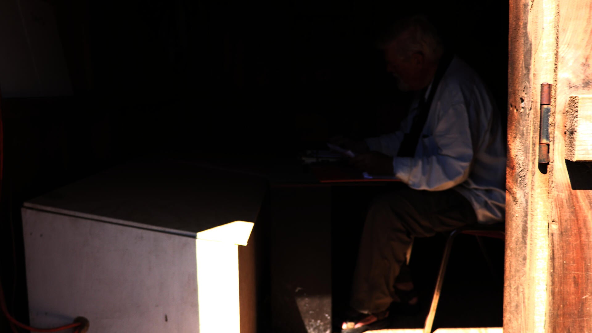 Man sits at a table in a wooden shed in Cape Cod MA recording the wave information.