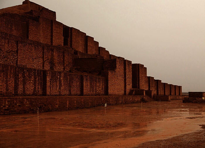 color photograph of the Choqa Zanbil ziggurat. The stepped, square building made of beige stone rises up imposingly from the beige sand.