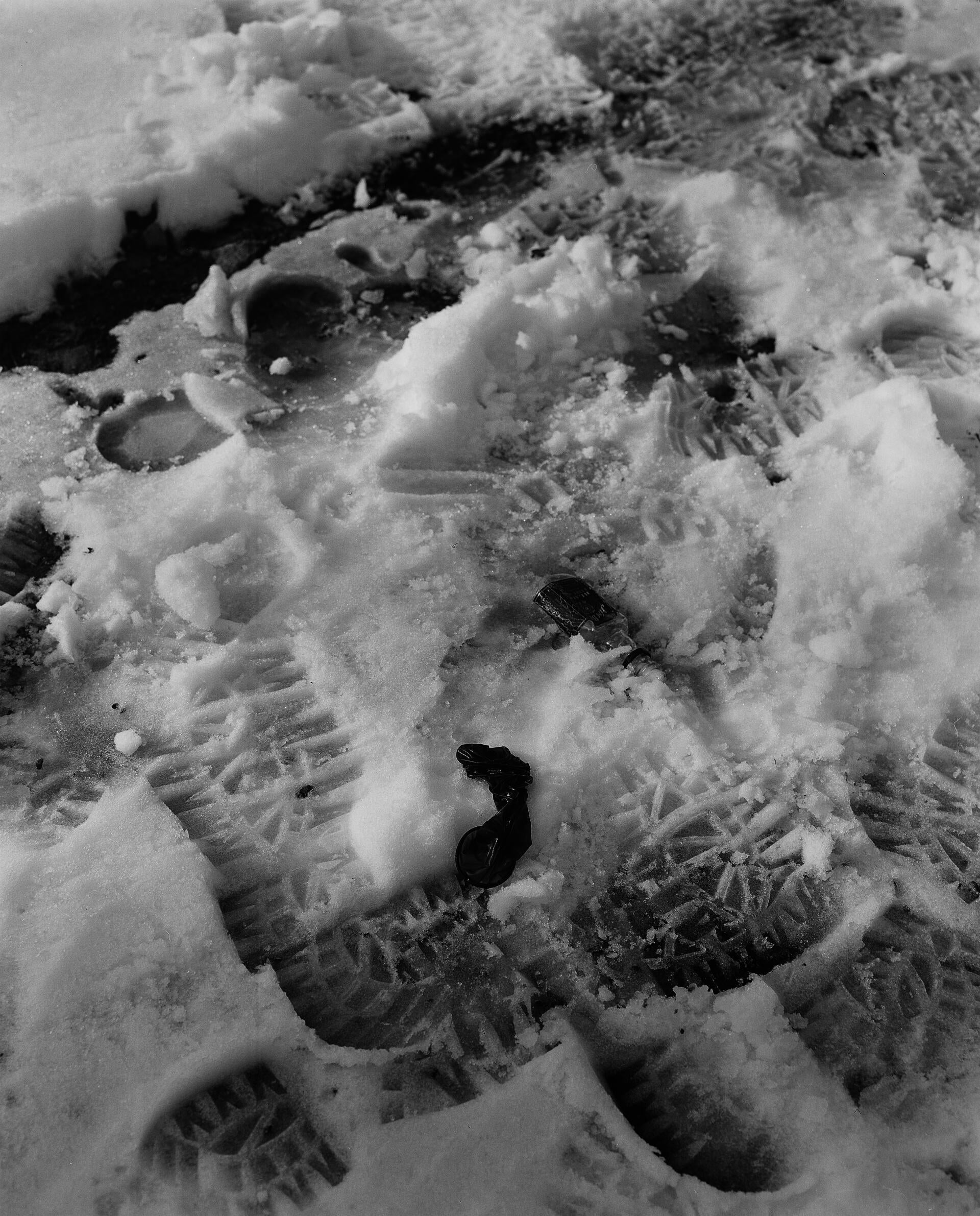 a black and white vertical image showing a used condom on top of foot prints in the snow 