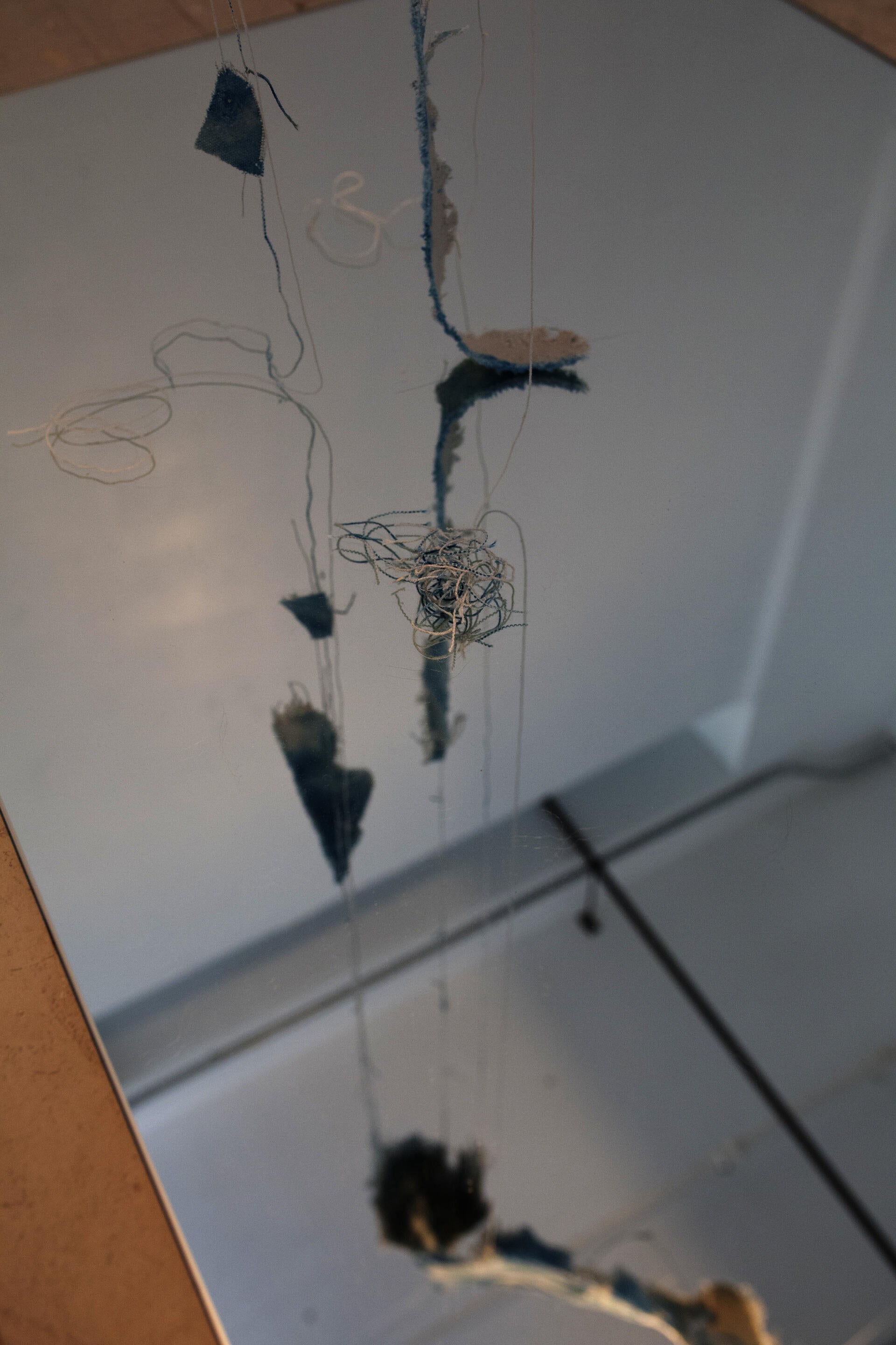 A reflection of beige canvas, dyed with spots of cyanotype is twisted and suspended in the air. The edges of the canvas have been unraveled and hang downward. 