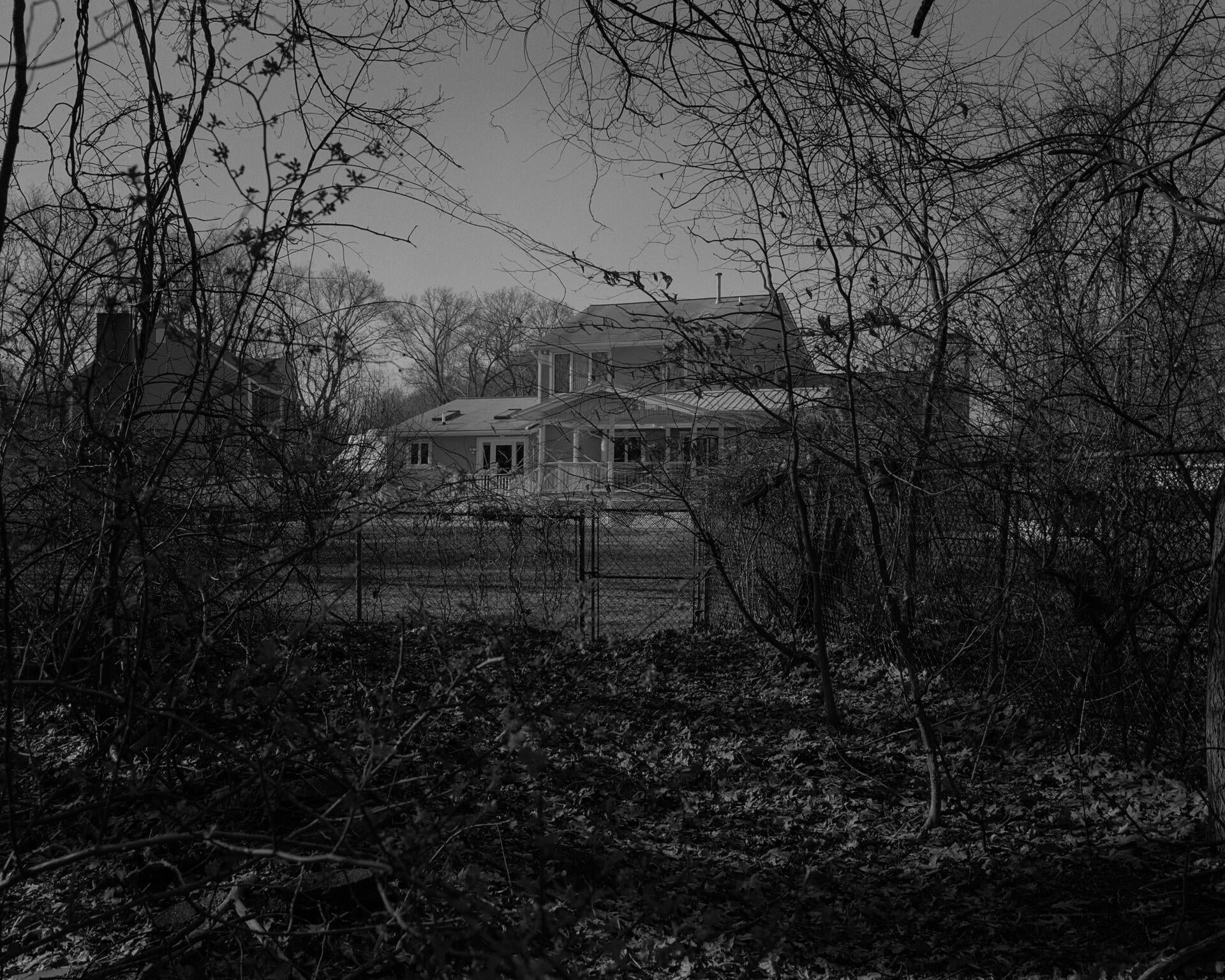 A black and white image of a house in the background hidden in the forest