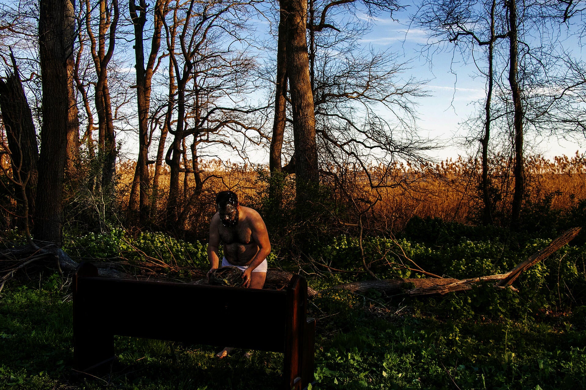 Photograph of artist in forest holding handmade nest made out of clay with plastic  silver confetti on his face. 