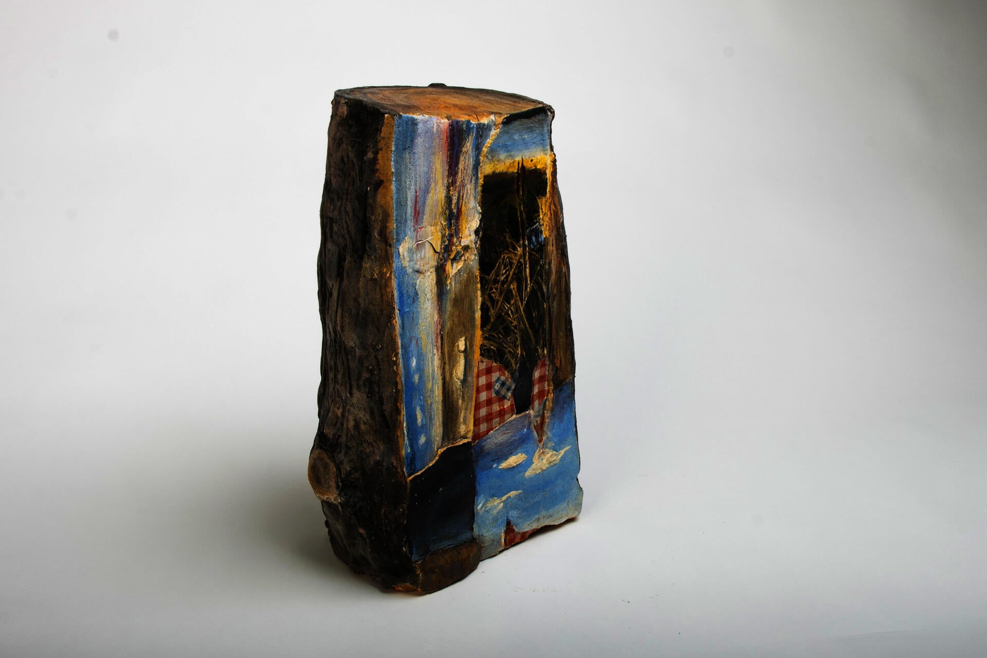 Ceramic piece resembling a cut log. The cut side of log has collaged images of the sea, cattails, and clouds.