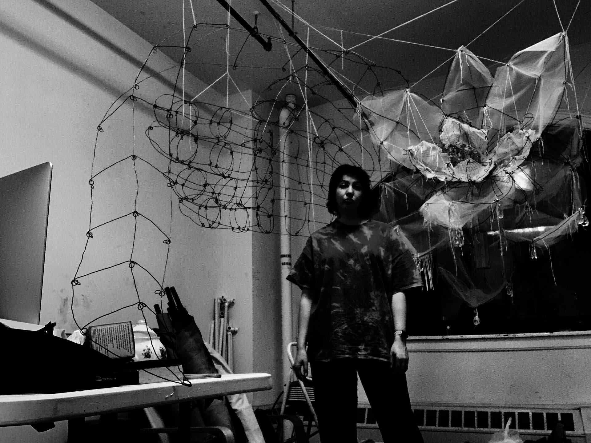 Hannah Suzanna standing in front of some of her partially completed wire sculptures, including a blade of grass, a hand, and a magnolia. - The Ephemeral Altar & The Floating Grave - Hannah Suzanna