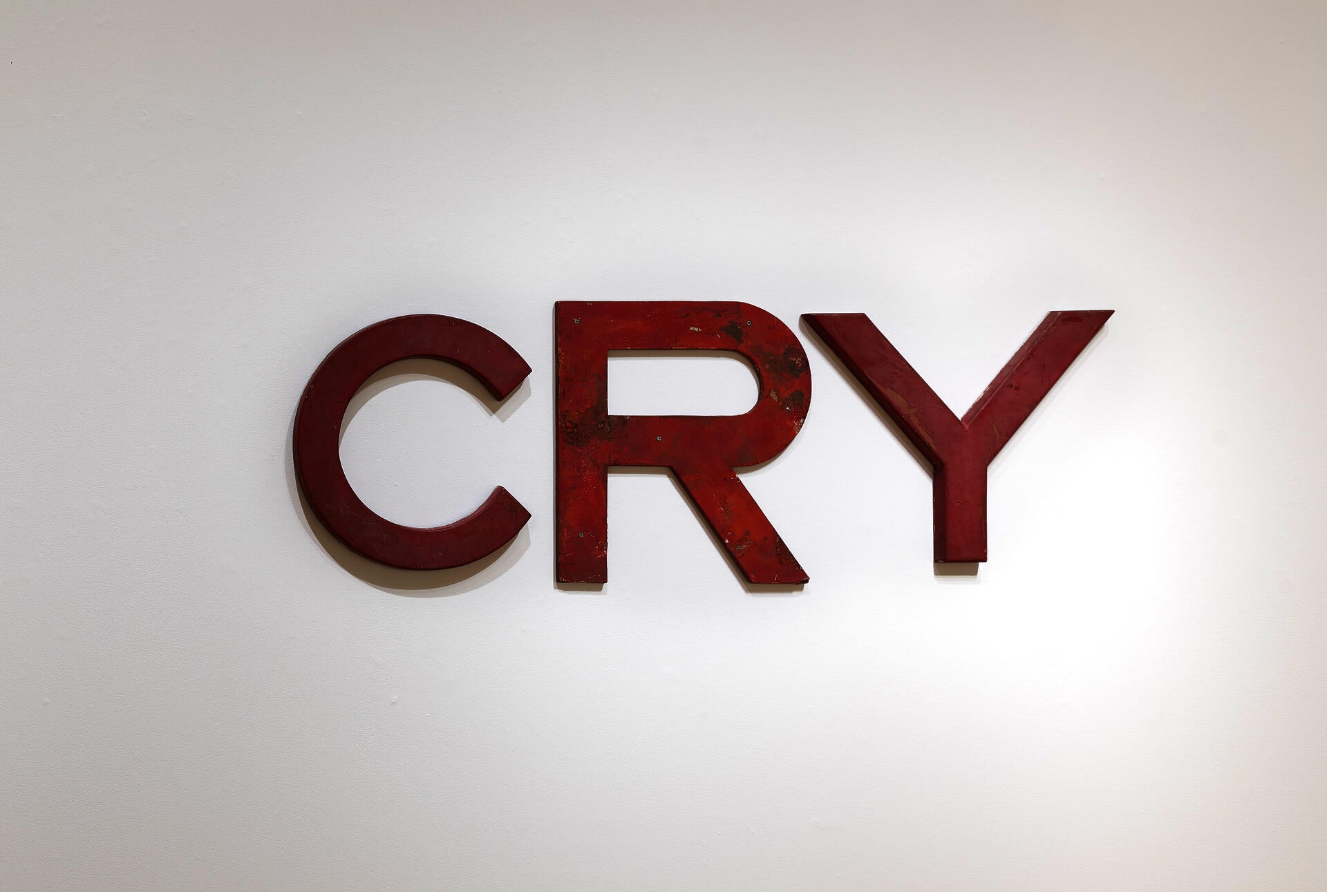 Slightly mismatched red san-serif letters mounted to a wall. They spell the word CRY.