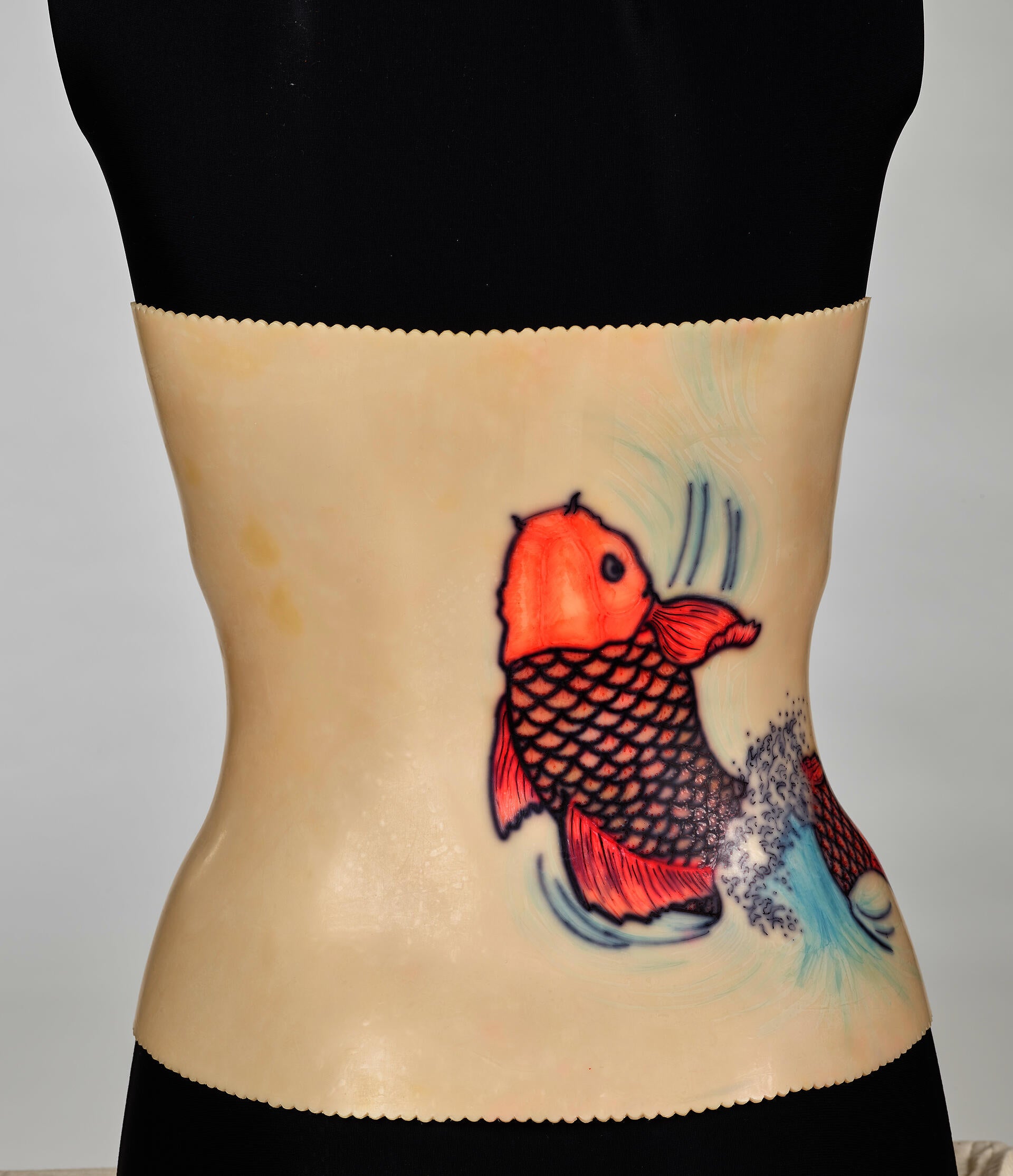 An off-white back brace is molded onto a black mannequin torso. The plastic brace attaches down the middle of the torso. A red koi design decorates the right side.