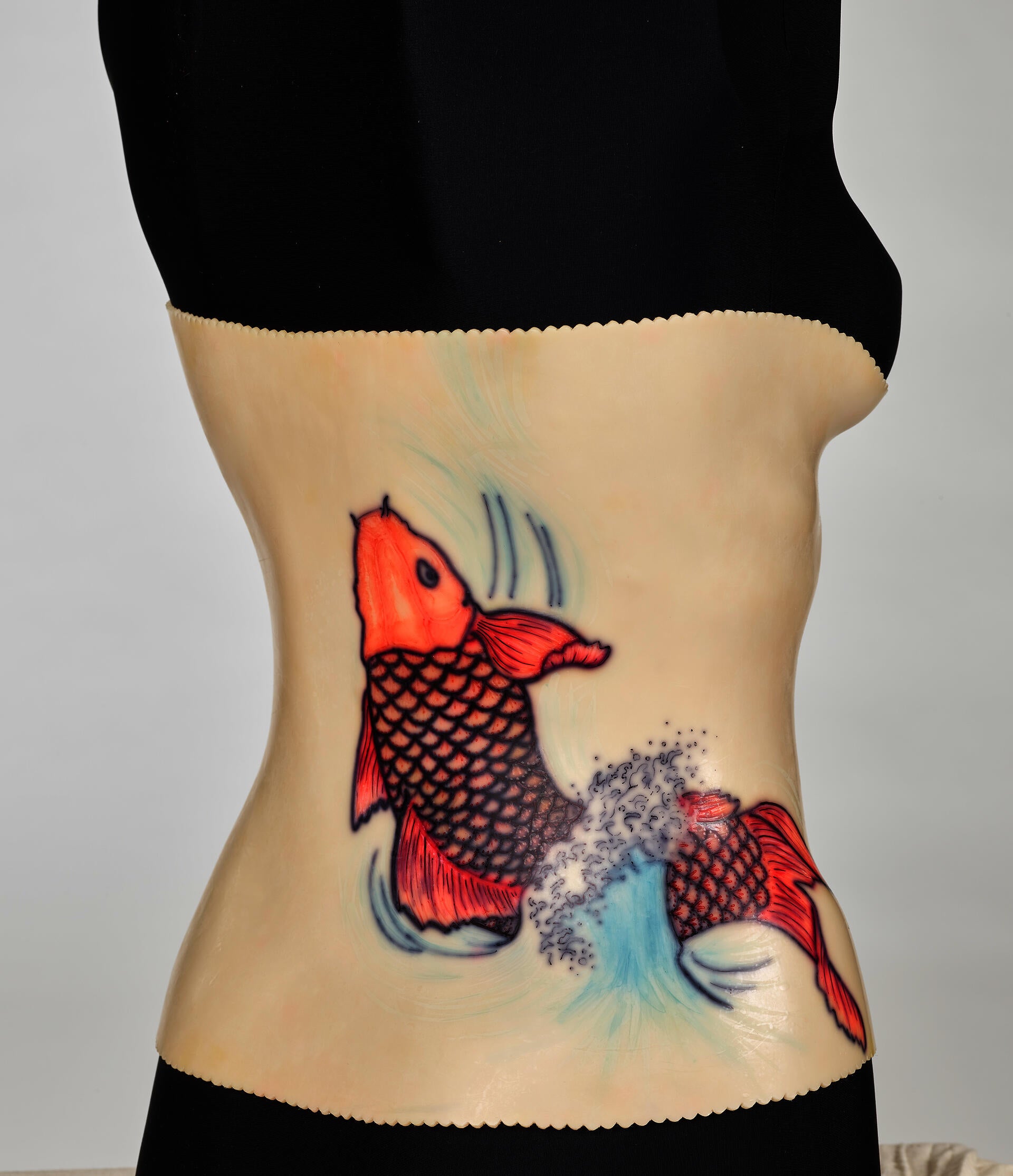 An off-white back brace is molded onto a black mannequin torso. The plastic brace attaches down the middle of the torso. A red koi design decorates the right side.