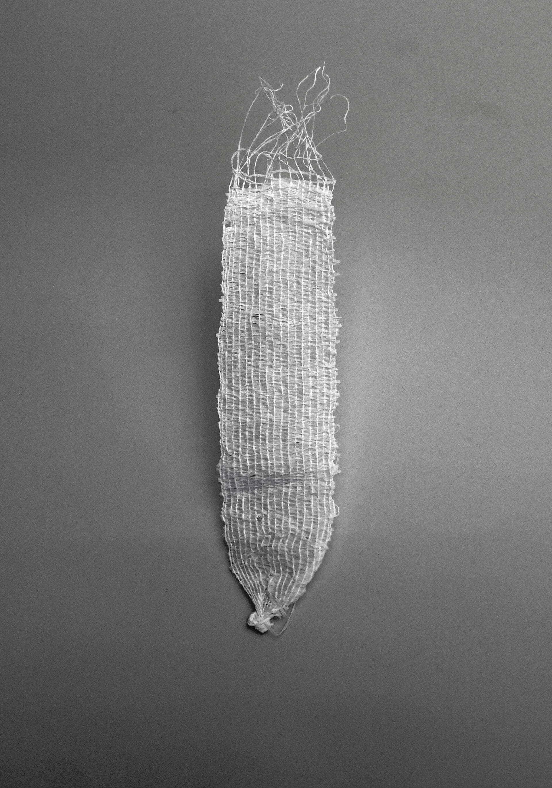 White, roughly woven strip which converges to a knot at the bottom. The top edges are frayed with loose threads.