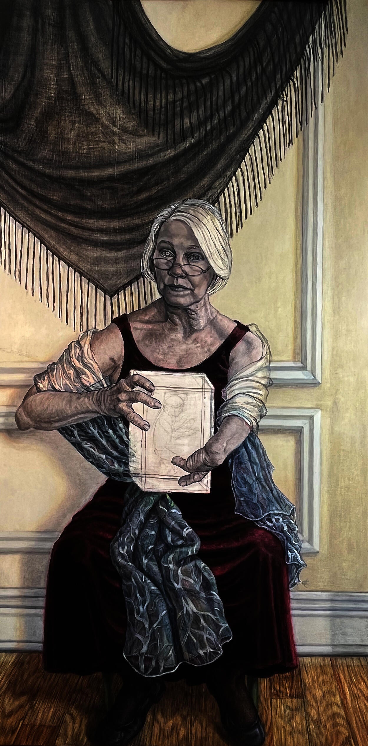 A seated elderly woman grasps a box with her hands, which have only a few fingers each. Only the box and her arms are painted as outlines.