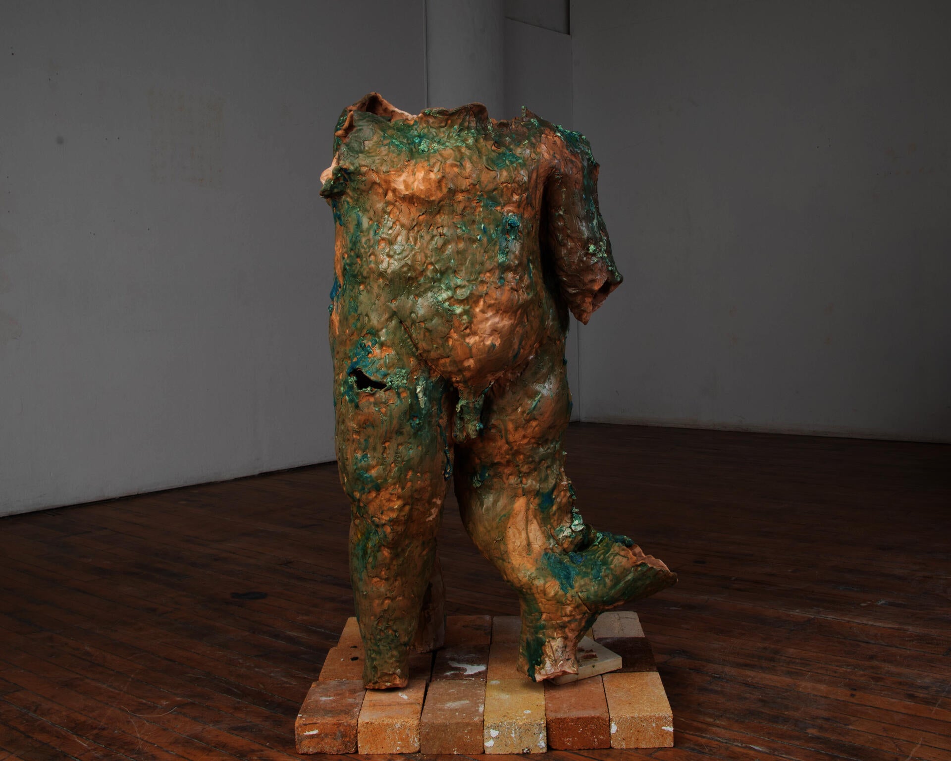 An enlarged and abject, hollow, ceramic body standing on top a small plinth of bricks