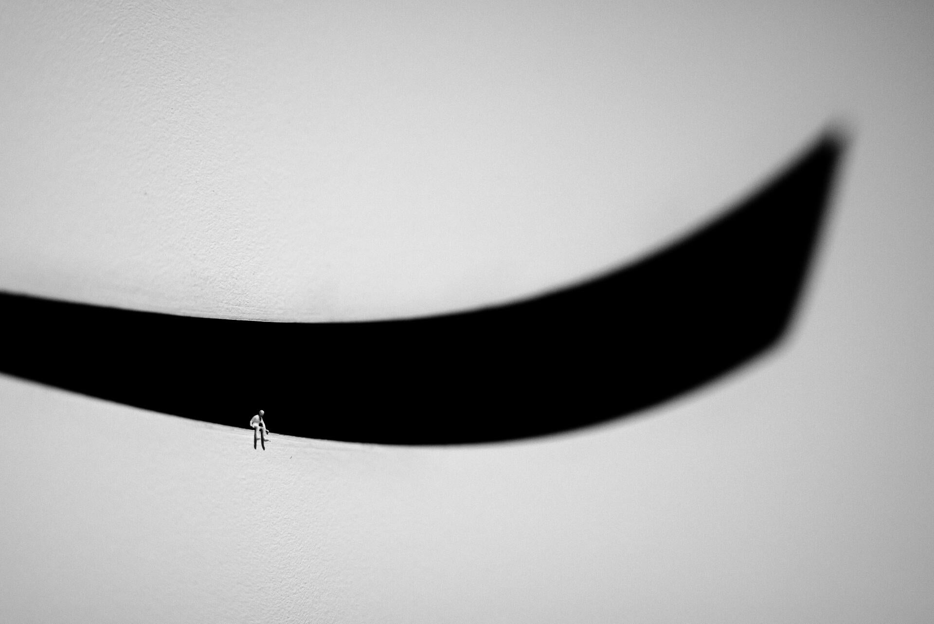 A black and white image of a colorless person sitting on a black curve.