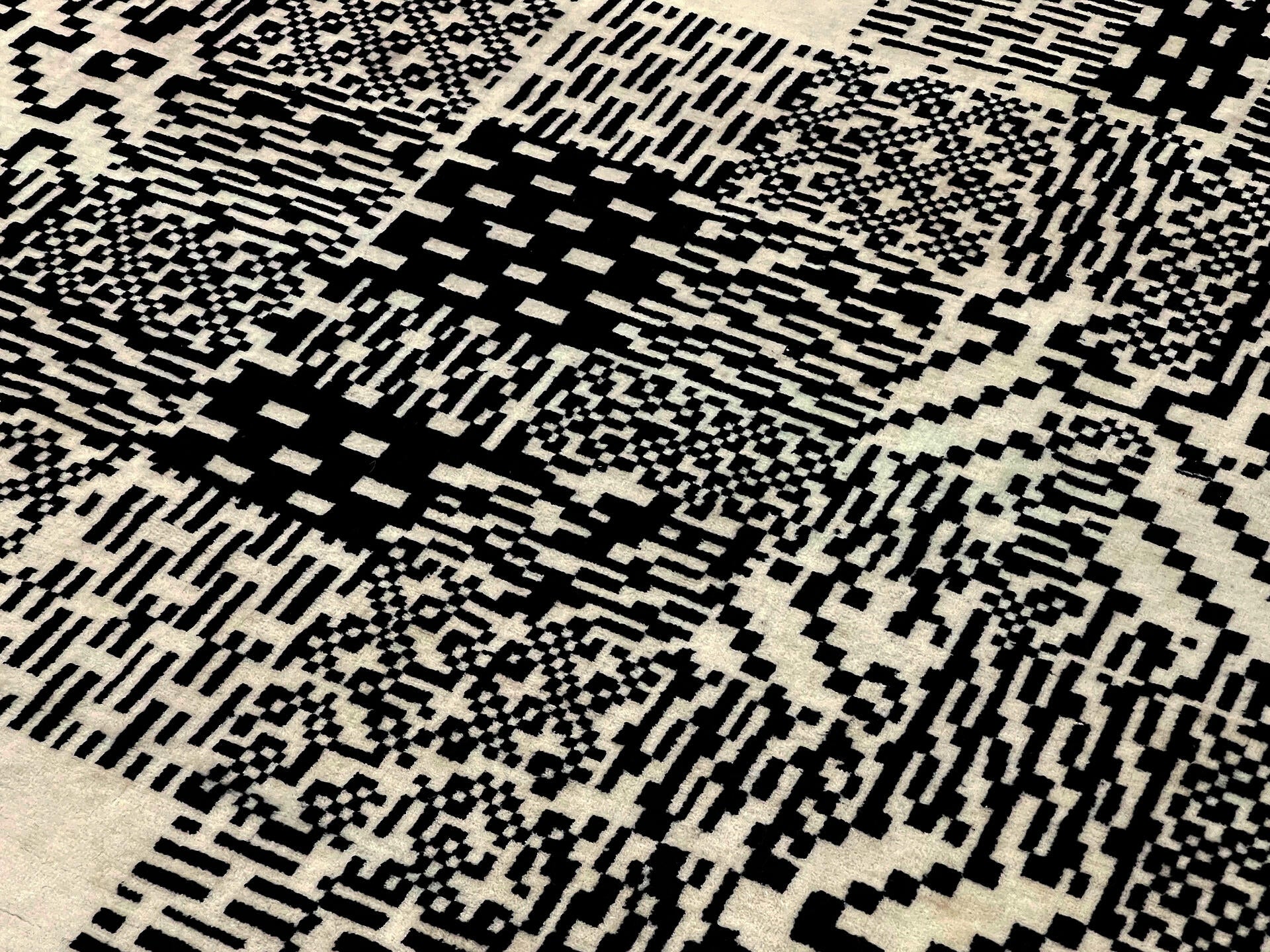 Detail documentation photograph of hand-knotted wool rug. The rug is covered in a semi-repetitive black and white patterned square image.