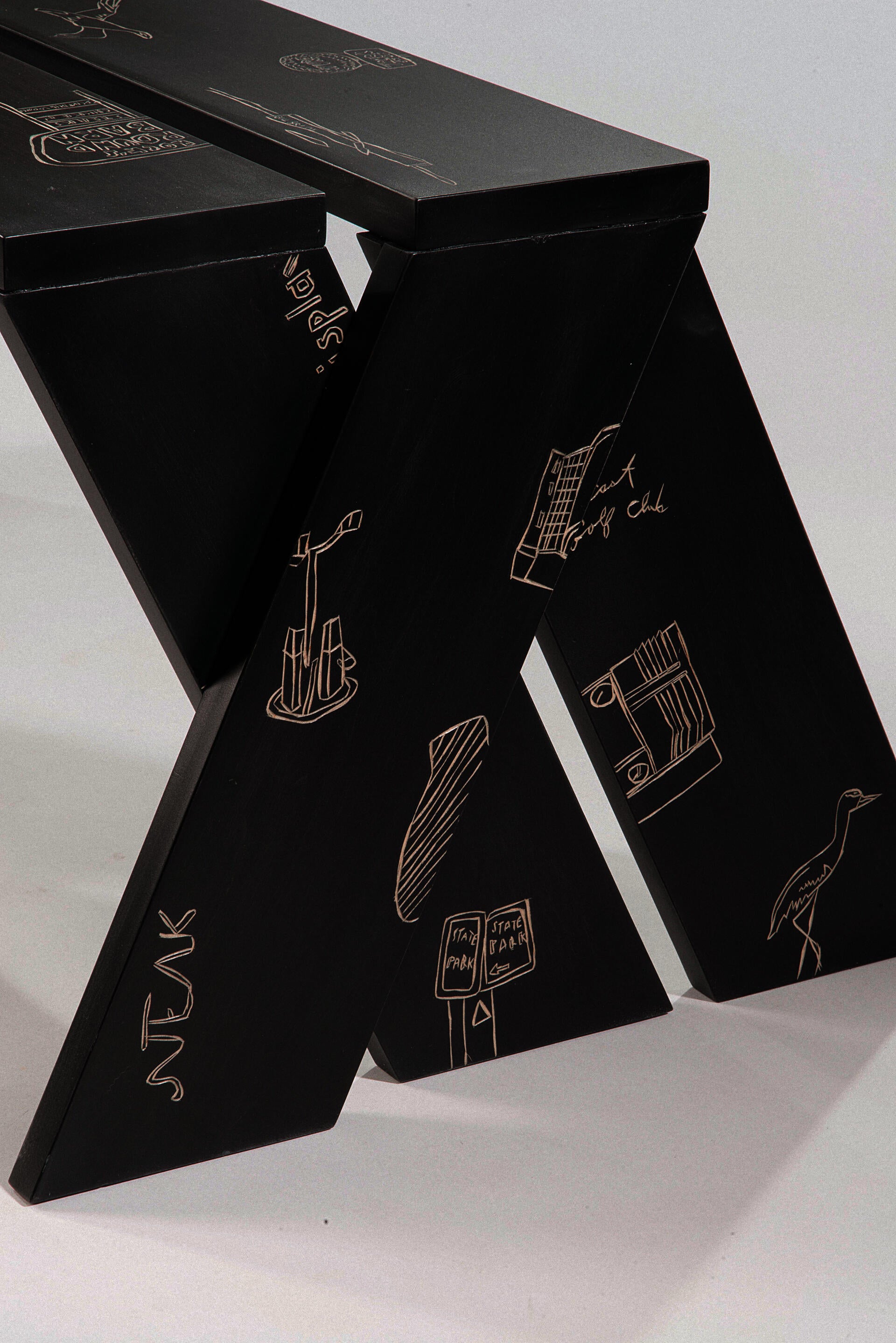 a black, planar solid wood bench covered with hand carved illustrations