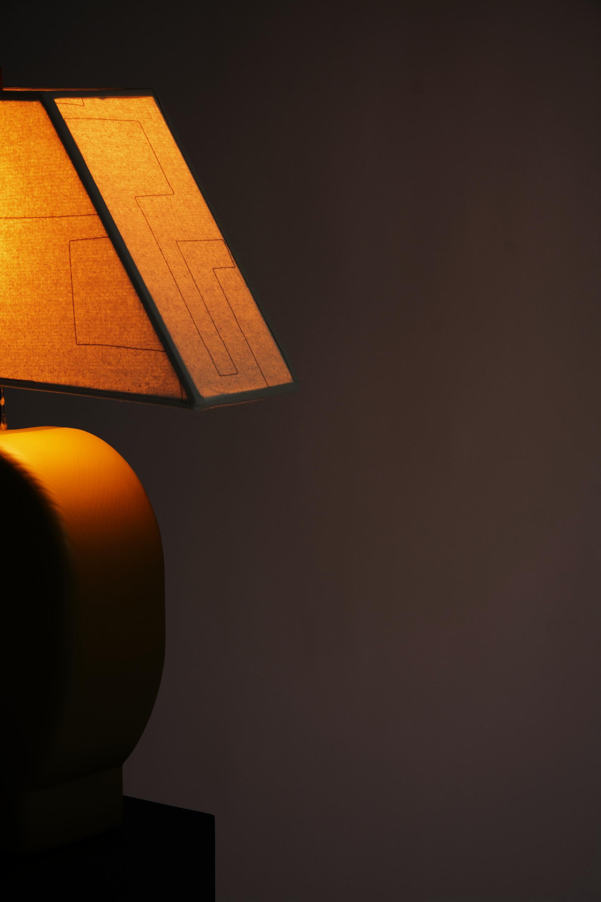 Detail view of Sister Lamp turned on, with an orange glow coming through the canvas shade.