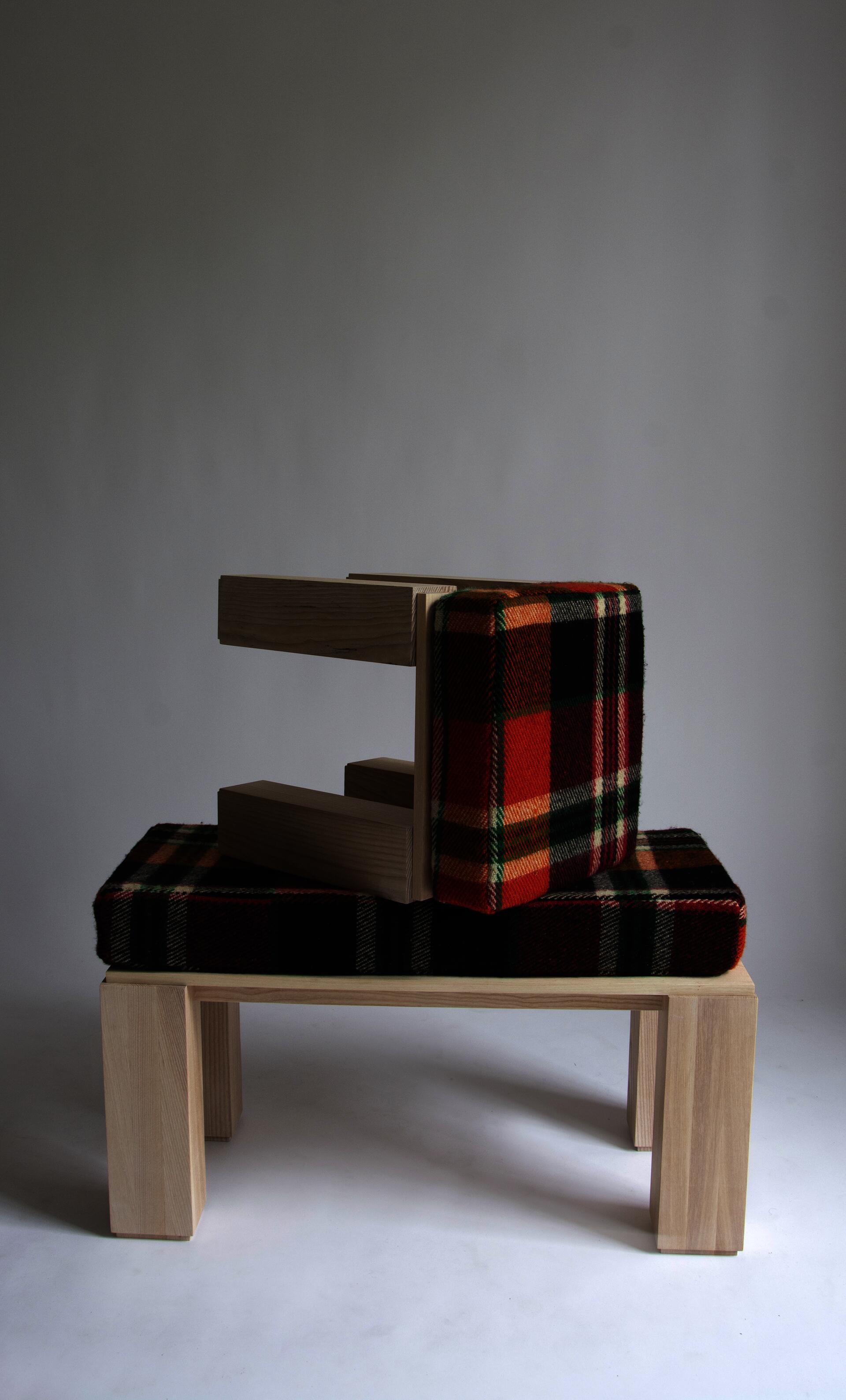 Wooden stool with orange, green and red plaid wool cushion sits kneeled on top of wooden bench with same plaid cushion.