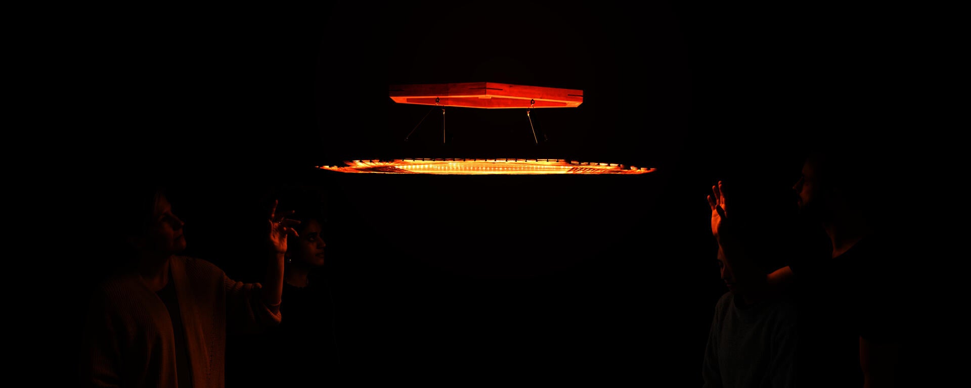 A chandelier with a dim warm light. 4 mesmerized individuals.