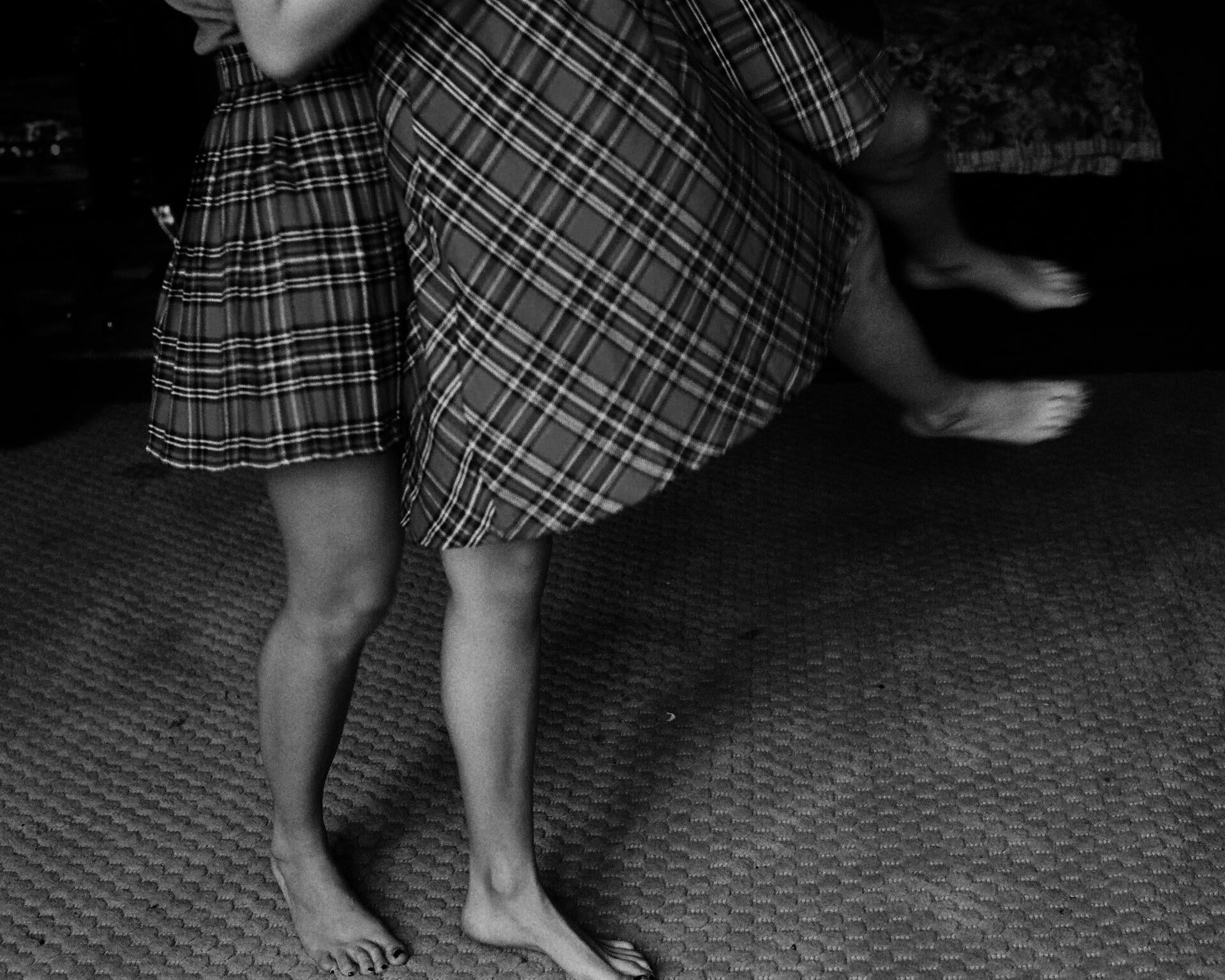 two pairs of legs in skirts, one flying the other, the flying feet blurred