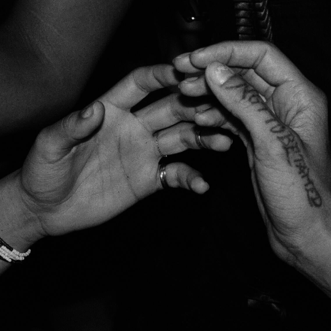 two hands only just touching or very nearly touching, the phrase "not to be tamed" tattooed along the thumb of one hand