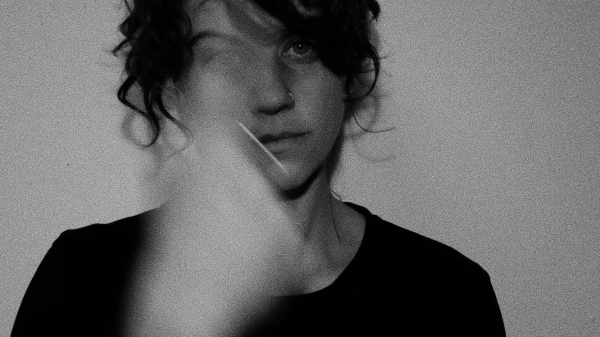 A black and white self portrait with my hand blurred as it moves between pointing at my head and at my heart.
