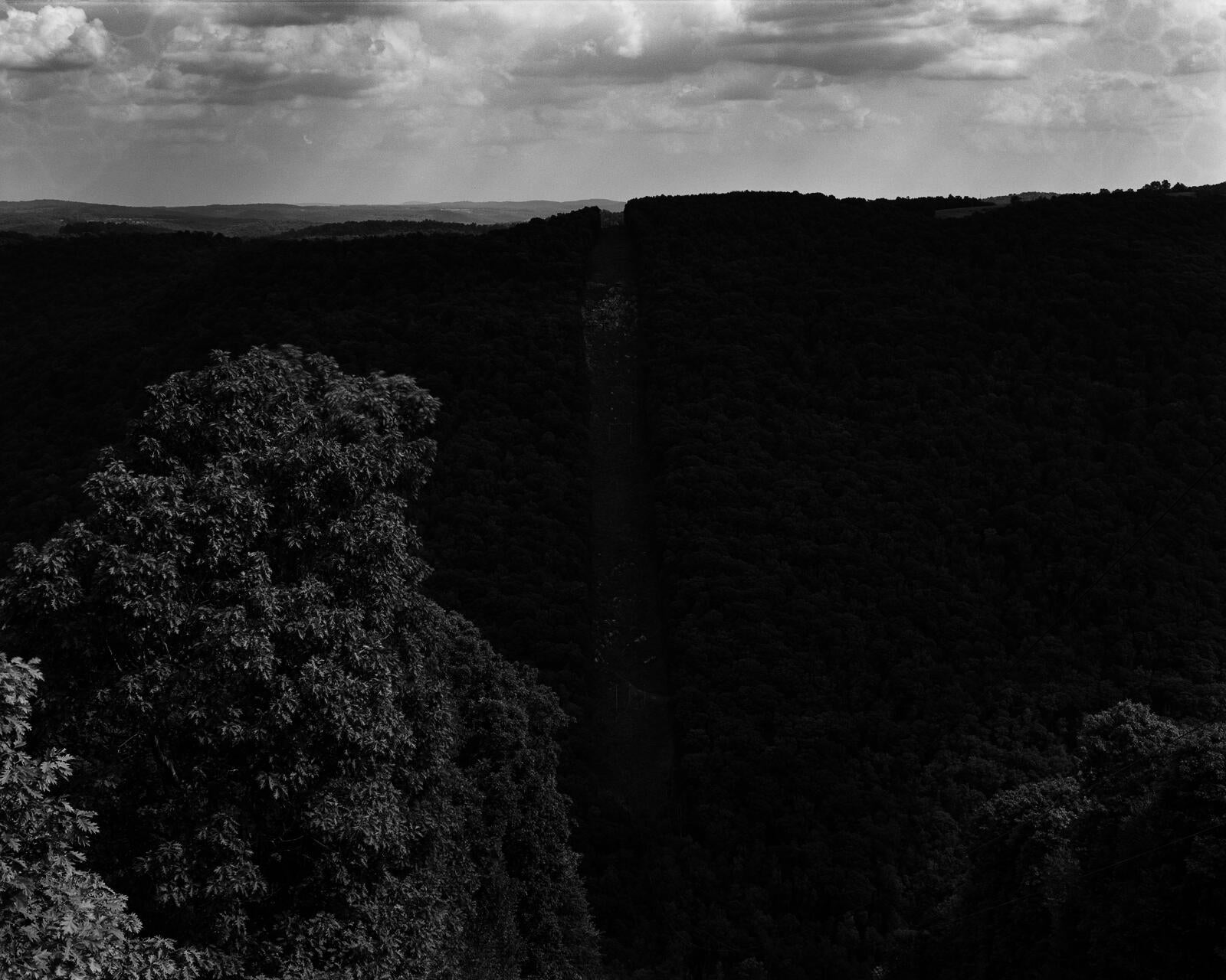 A landscape from the top of a mountain looking down into a valley. Down the middle of the image runs a cleared corridor for power lines.