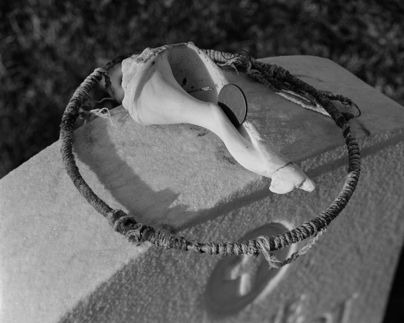 A gravestone is topped with a wooden hoop and a conch shell.