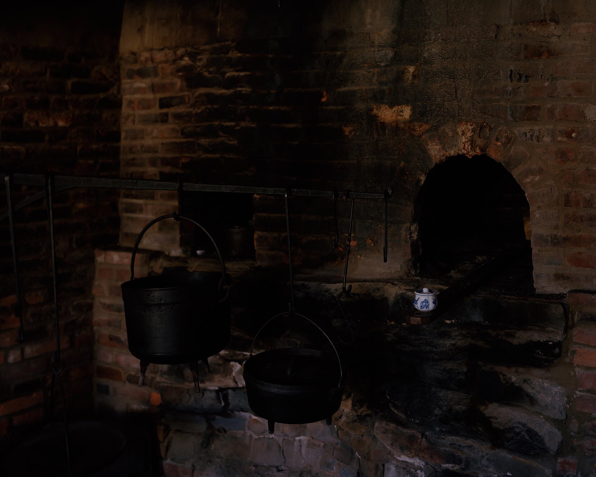 Photograph of brick oven hearth, with three cast iron pots hanging from a large rod.