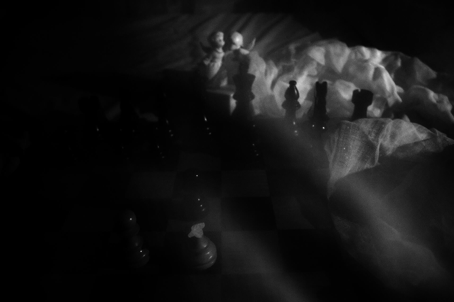 Chess board sitting on top of bed sheets a long with two porcelain angels in the background.