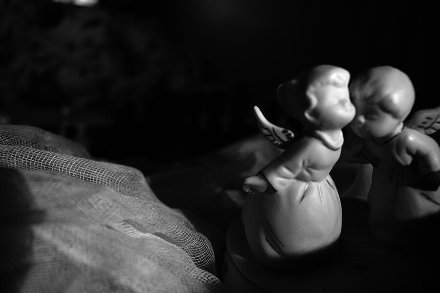 Chess board sitting on top of bed sheets a long with two porcelain angels in the foreground.