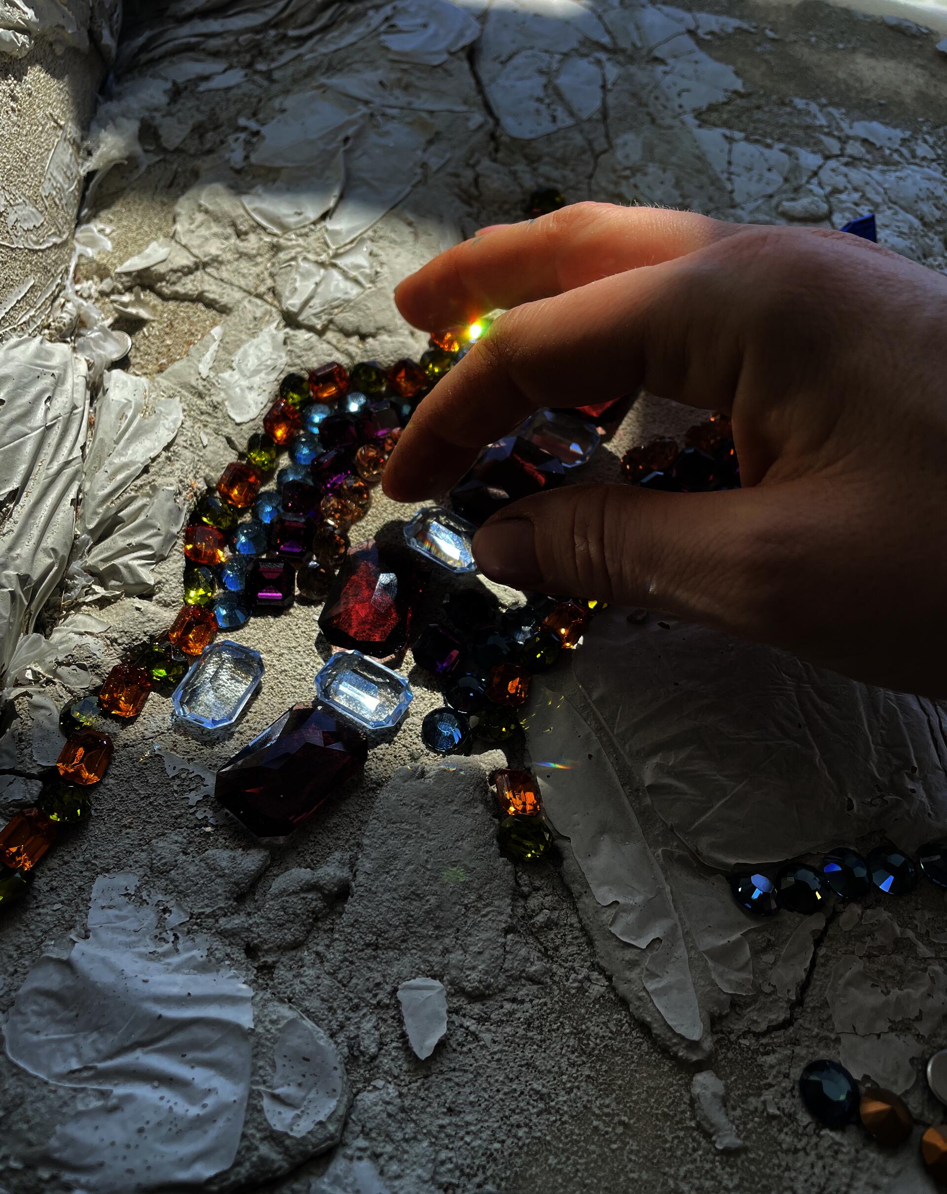 Sunlight piercing various colors of crystals casts rainbows onto a hand.