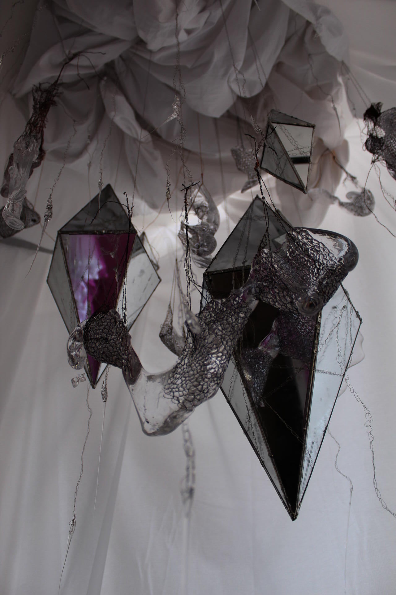 Mirrors in the shape of diamonds hang from the ceiling along with glass pieces.  All are suspended by metal crochet weavings.