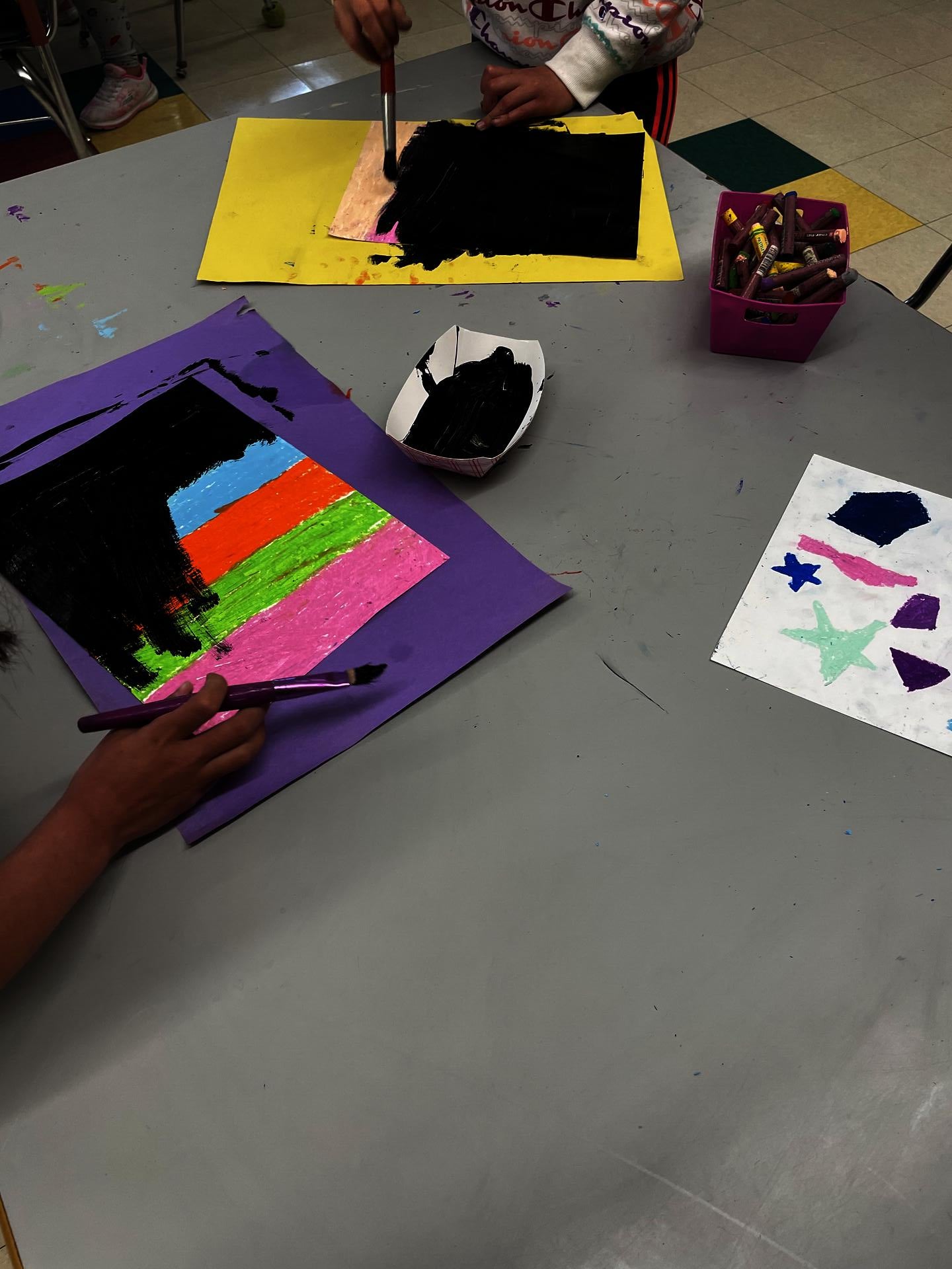 Students cover oil pastel colors with tempera paint to prepare for etching. 